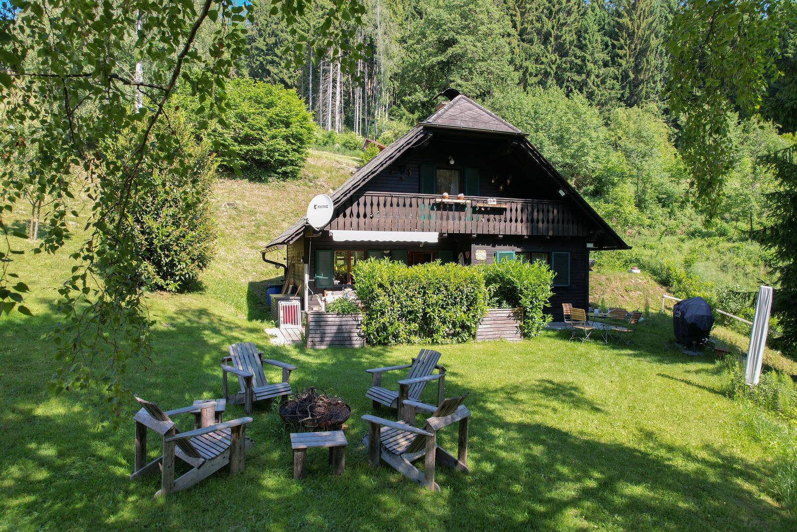 Traditionelles Holzhaus mit großem Garten, Feuerstelle und Sitzgelegenheiten im Grünen.
