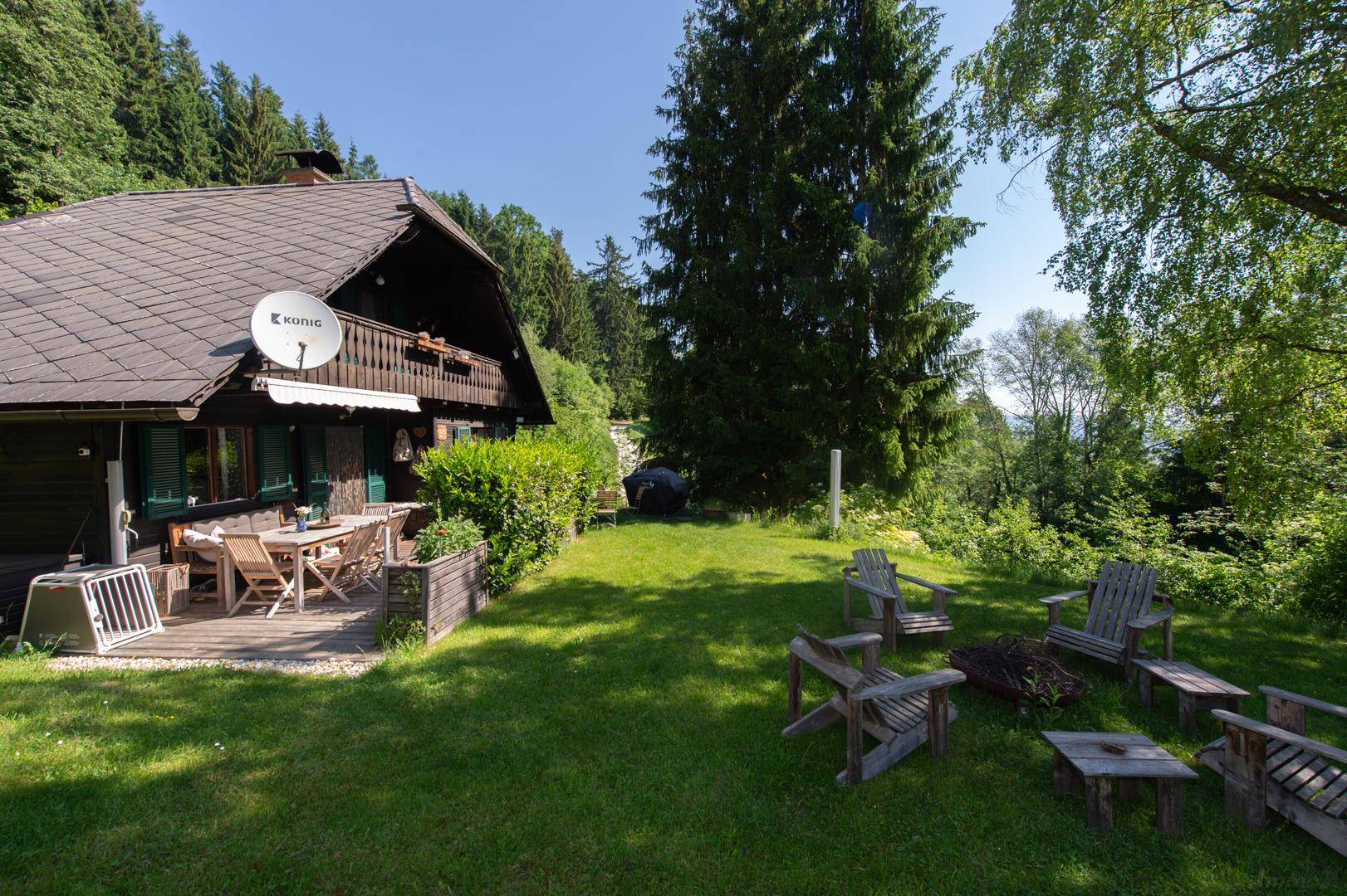 Weitläufiger Gartenbereich mit Feuerstelle und einer Terrasse mit Esstisch am Holzhaus.