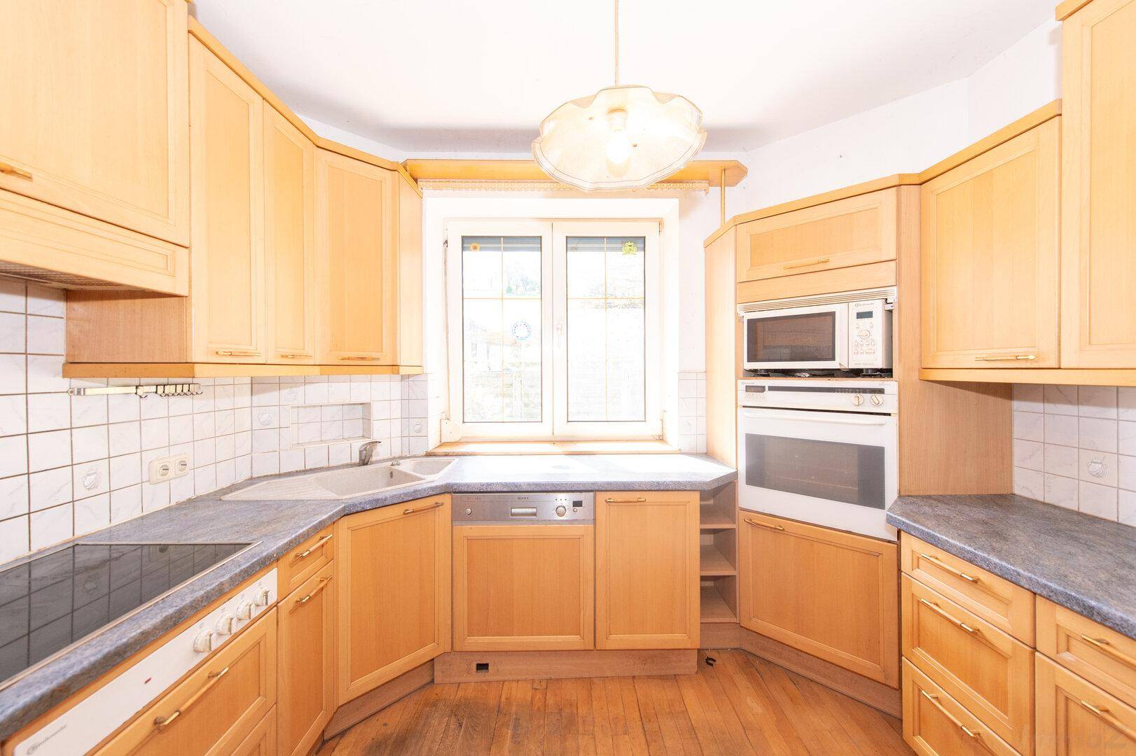 Helle Küche mit Holzschränken, Einbaugeräten und Fenster über der Spüle.
