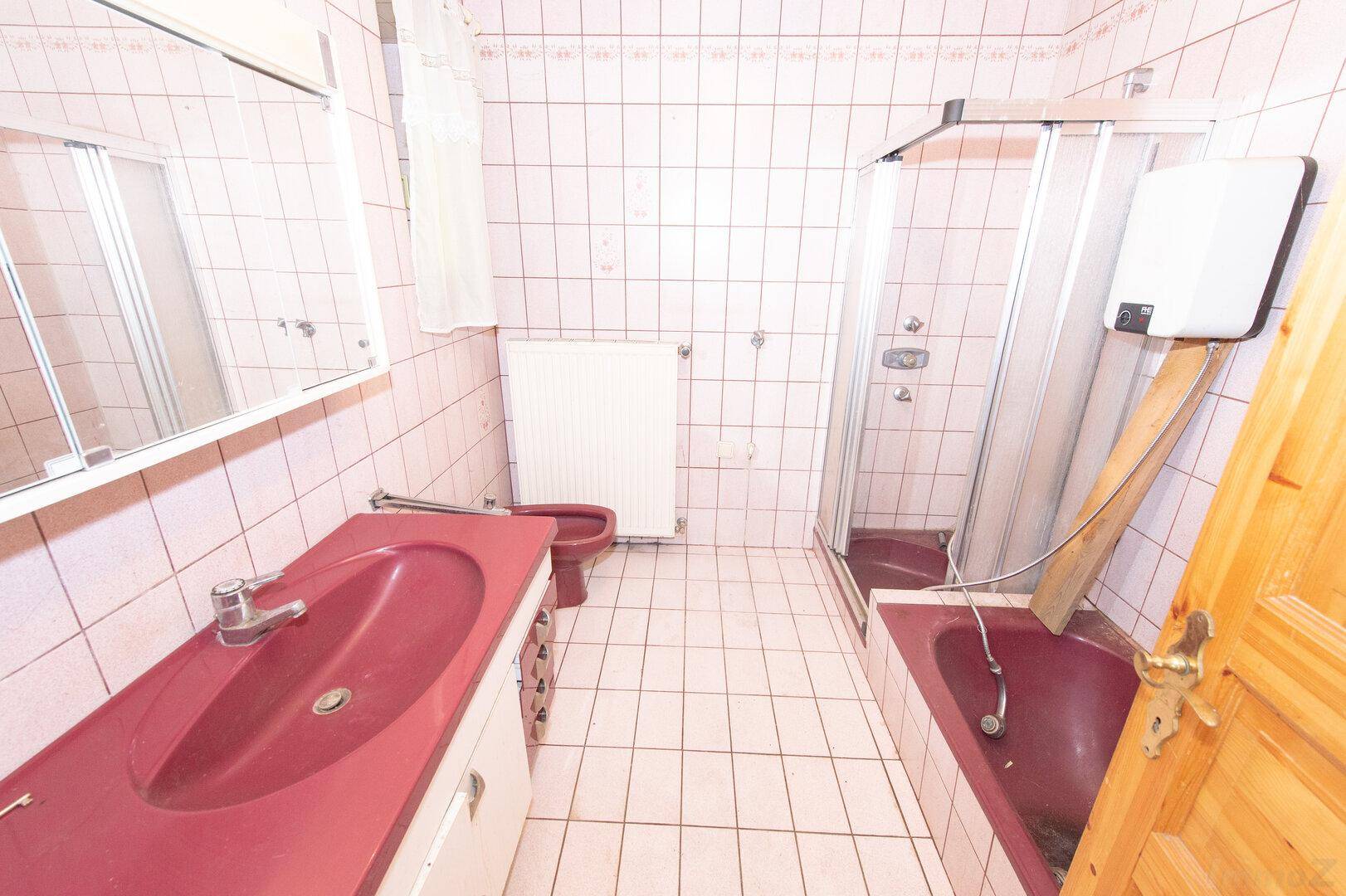 Badezimmer mit rosa Fliesen, Badewanne, Dusche und Doppelwaschbecken.