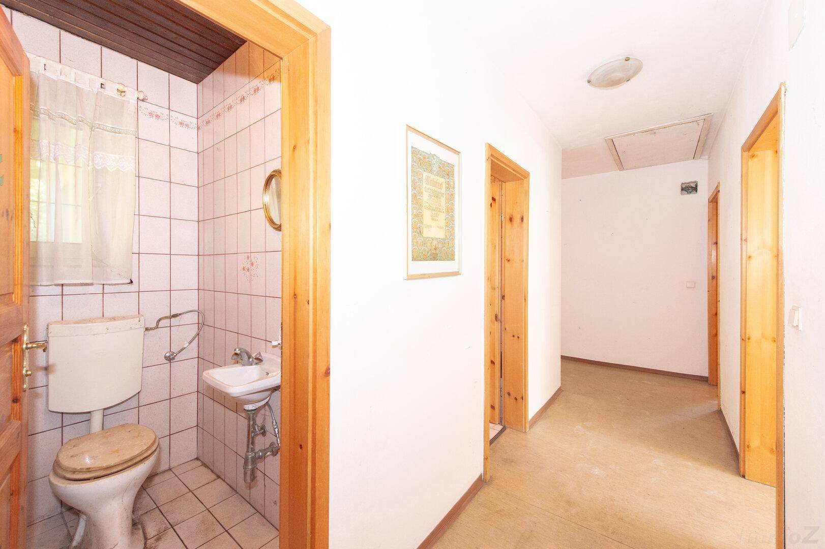 Kleines Gäste-WC mit Fliesenboden, Toilette und Waschbecken im Flur.