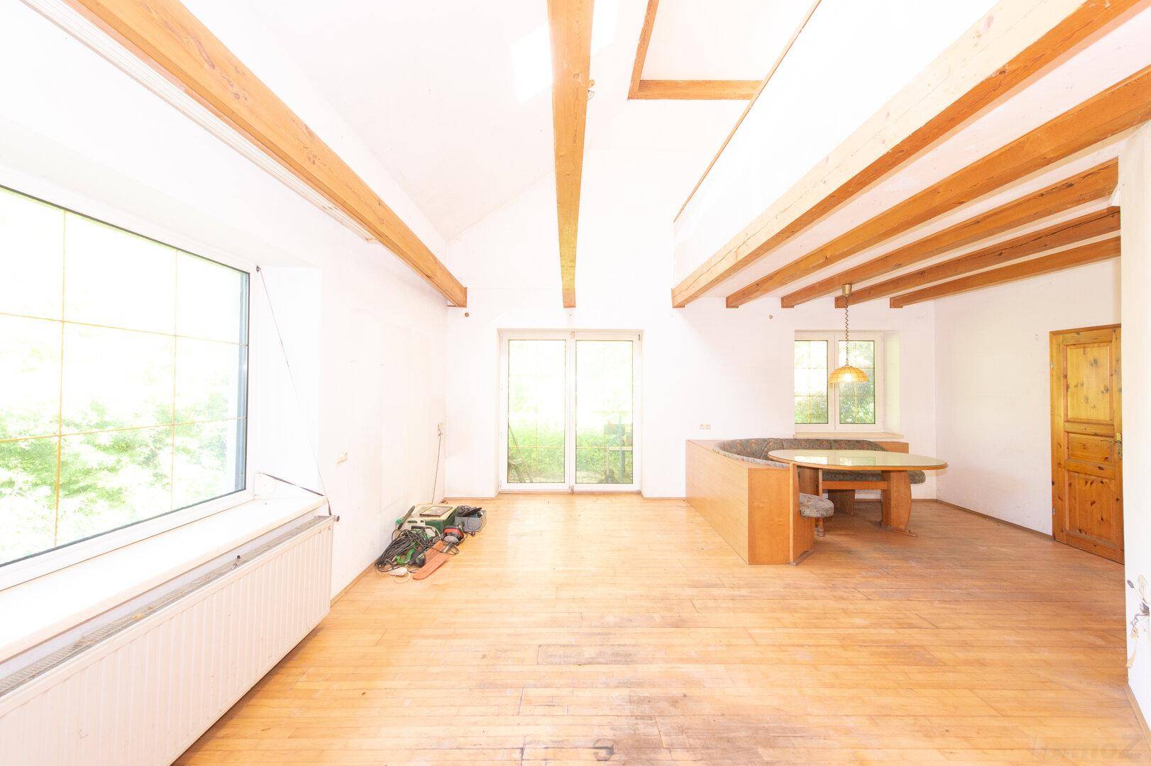 Offener Wohn- und Essbereich mit Holzbalkendecke, Holzboden und viel Tageslicht.