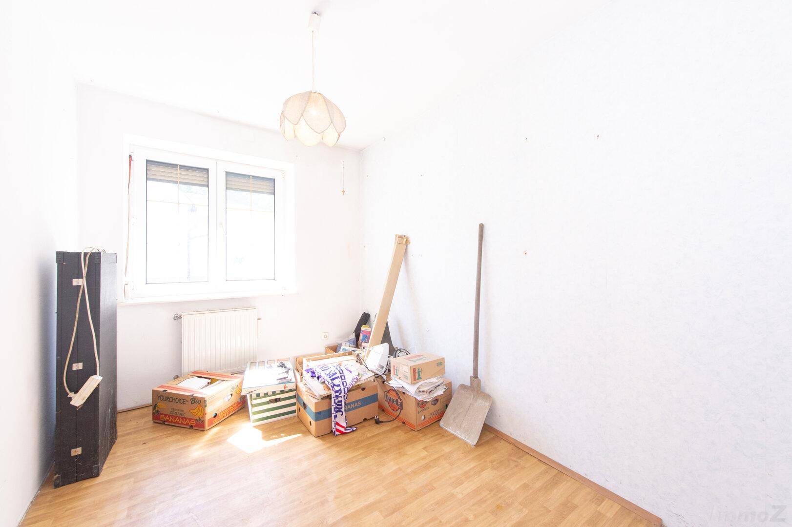 Leerer Raum mit Holzboden, Fenster und Heizkörper, bereit zur individuellen Gestaltung.