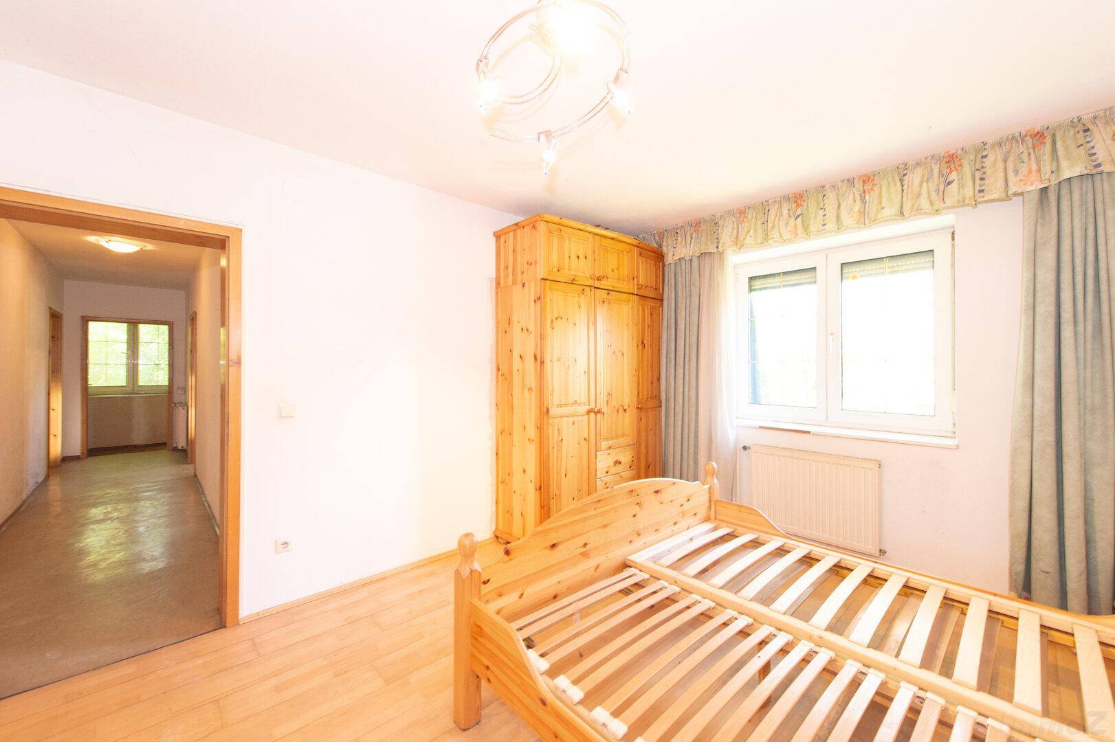 Schlafzimmer mit Holzbett, Kleiderschrank und Zugang zum Flur.