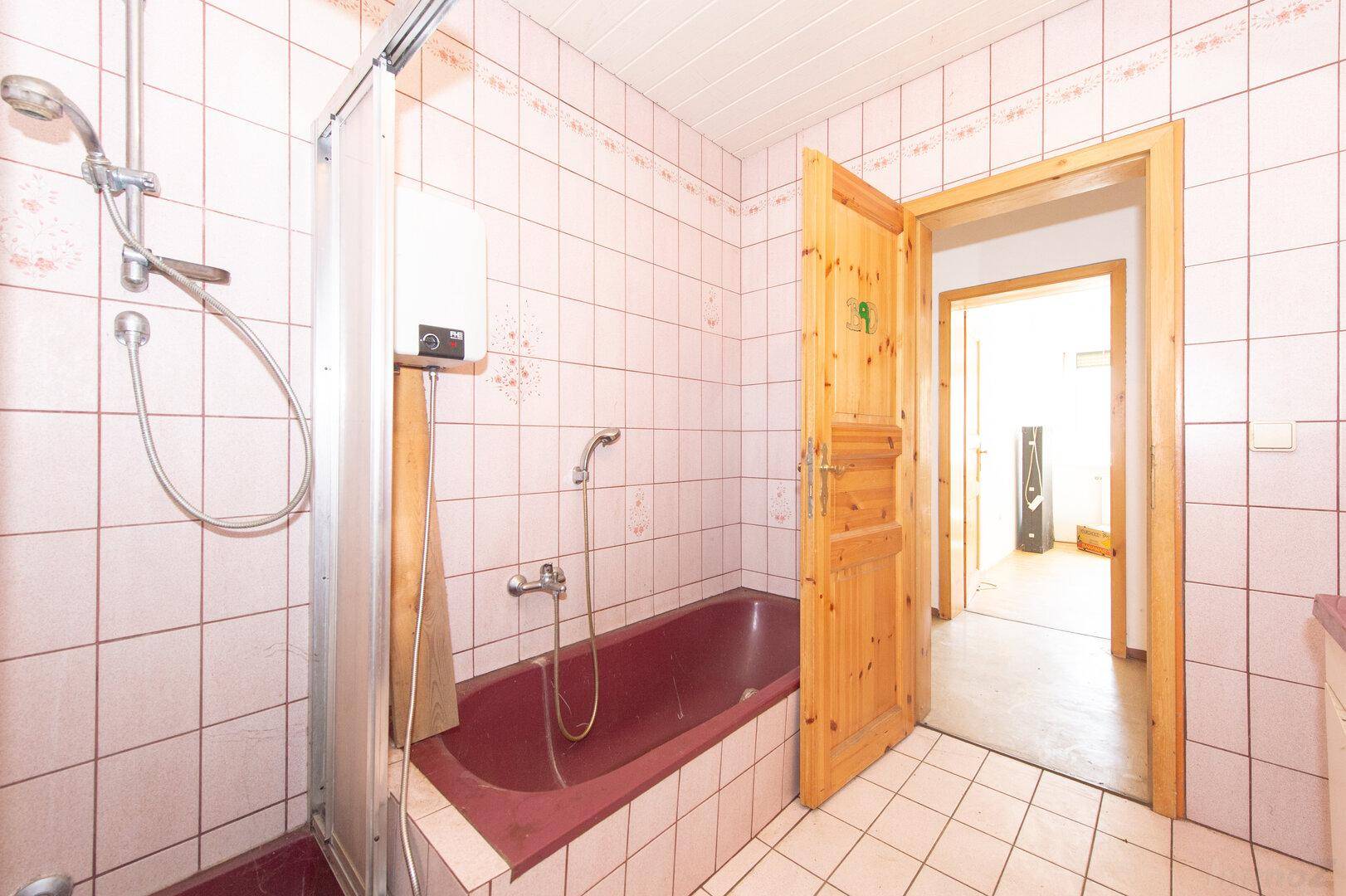 Badezimmer mit rosa Fliesen, Badewanne mit Duschvorrichtung und Holztür.