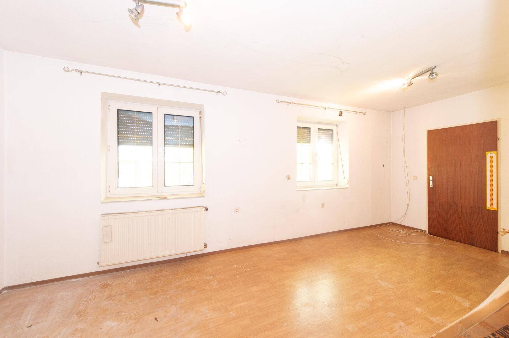 Leerer Raum mit Holzboden, zwei Fenstern und Heizkörper, bereit zur Nutzung.