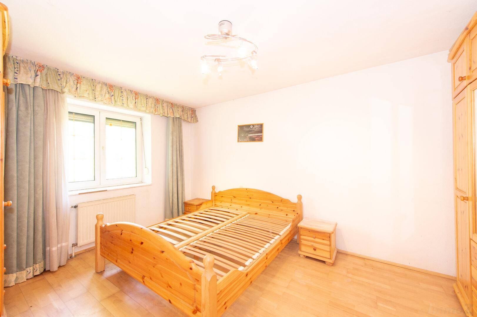 Helles Schlafzimmer mit Holzbett, Nachttischen und Fenster mit Vorhängen.