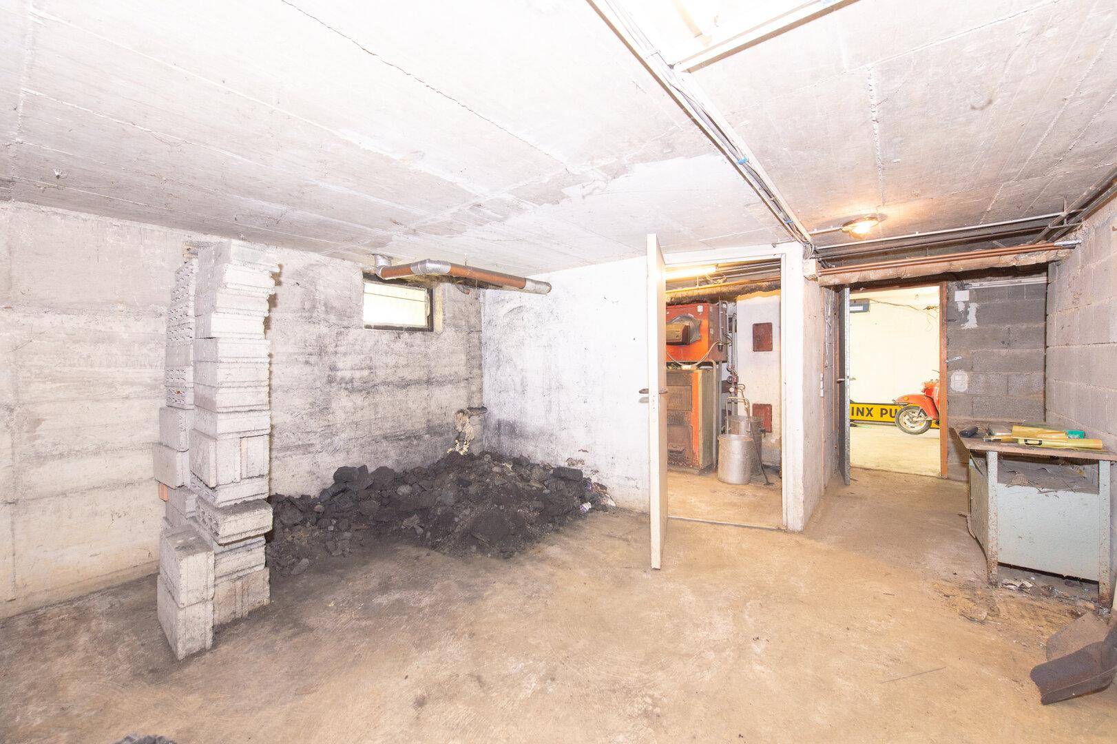 Unfertiger Kellerraum mit Betonwänden, Lagerfläche und Zugang zum Heizungsraum.