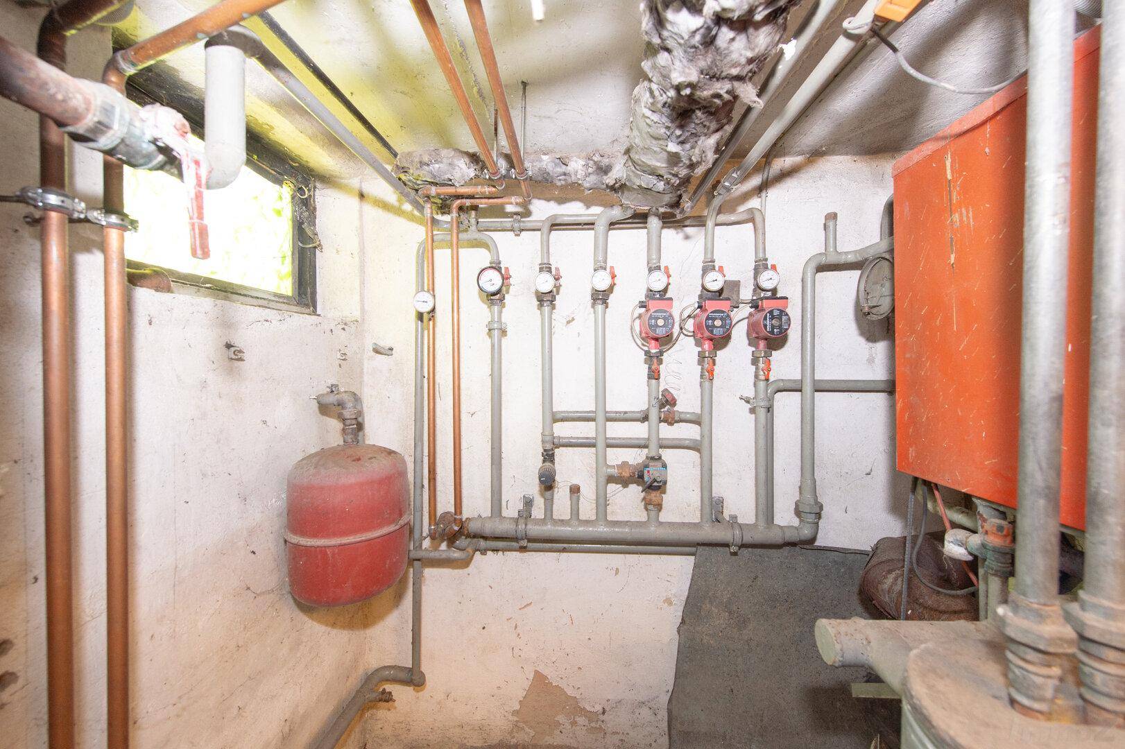 Heizungsanlage mit Rohren und Kesseln in einem funktionalen Kellerraum.