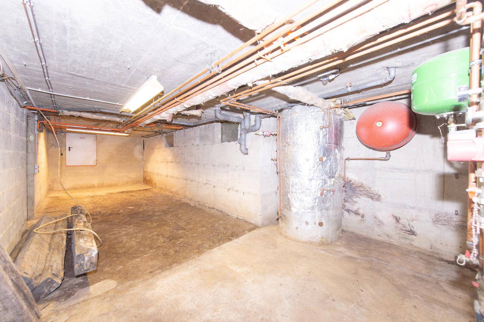 Geräumiger Kellerraum mit Betonwänden, Warmwasserspeicher und sichtbaren Installationen.