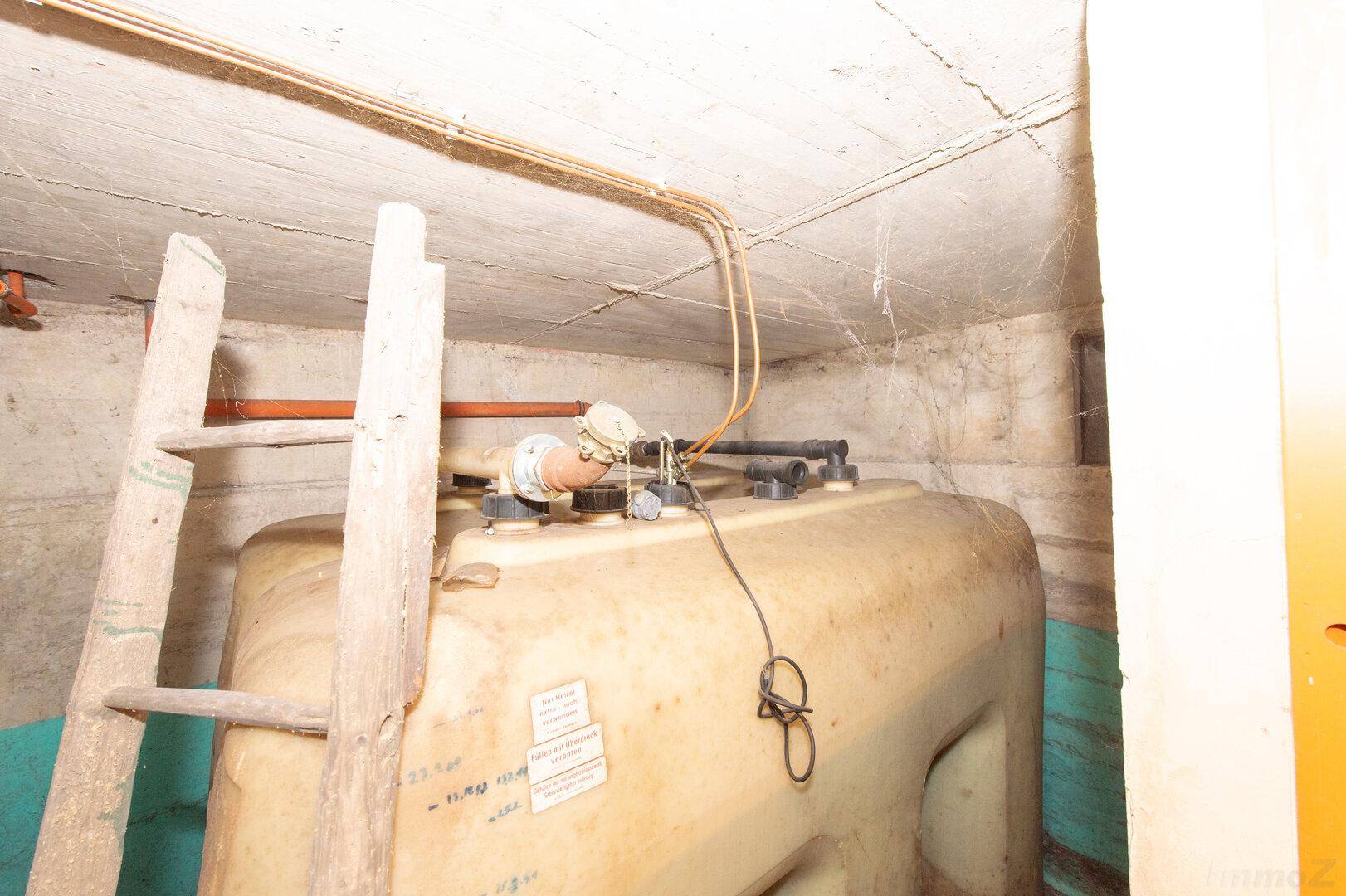 Großer Heizöltank in einem Kellerraum mit sichtbaren Rohren und einer Leiter.