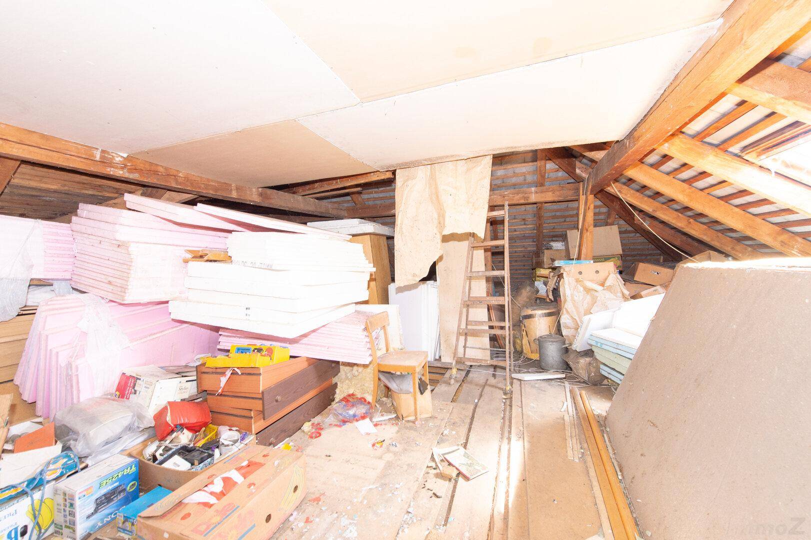 Unausgebauter Dachboden mit sichtbaren Holzbalken und gelagerten Baumaterialien.