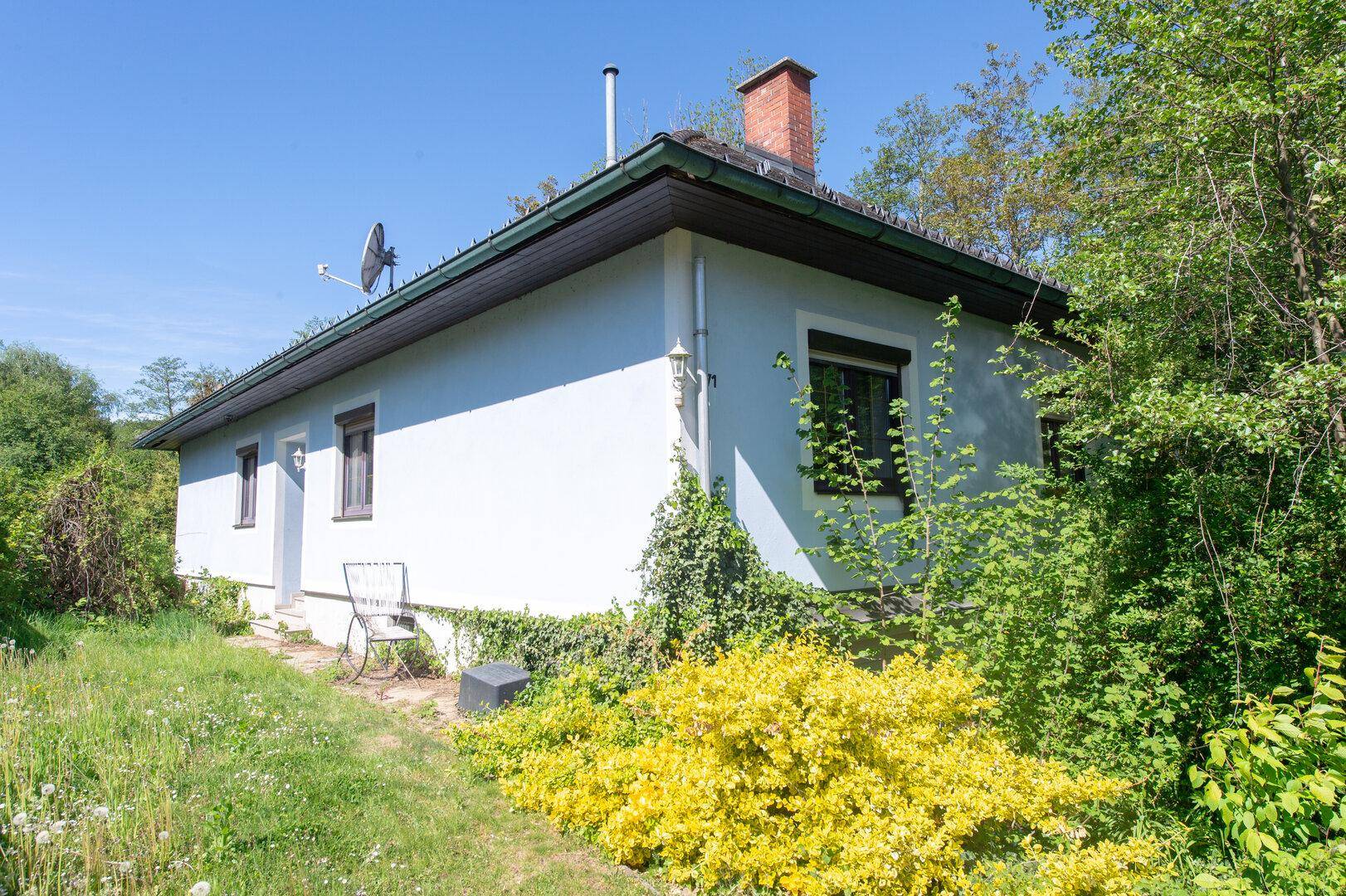 Helles Einfamilienhaus mit hellblauer Fassade und grüner Umgebung unter blauem Himmel.