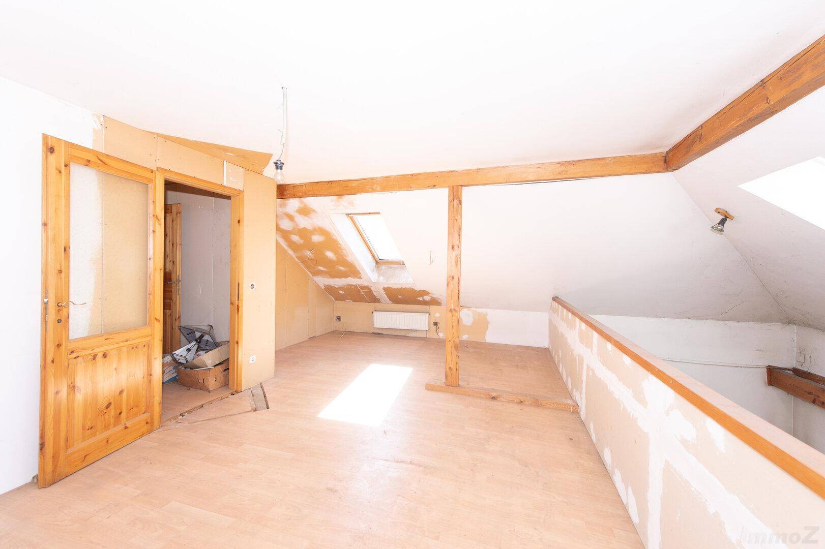 Heller Dachbodenraum im Umbau mit Holzboden, Dachfenstern und sichtbaren Holzbalken.