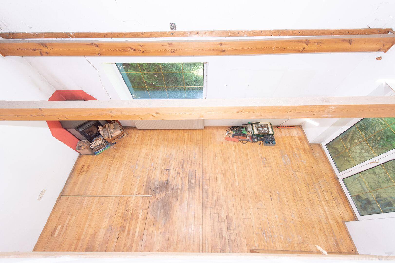 Geräumiger Wohnbereich mit Holzboden, großen Fenstern und sichtbaren Deckenbalken.