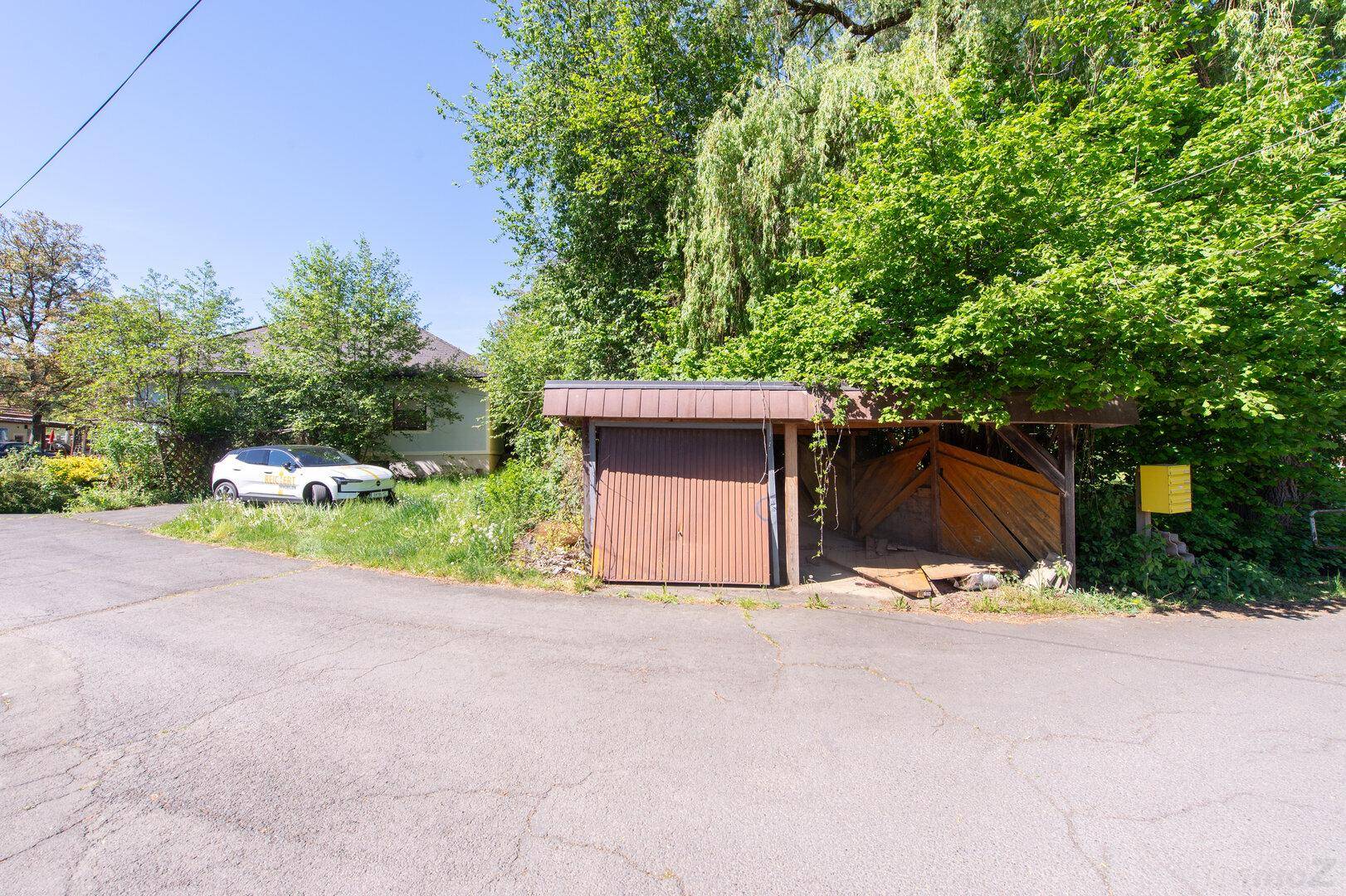 Kleine Garage und ein Carport, umgeben von Bäumen und einer grünen Umgebung.