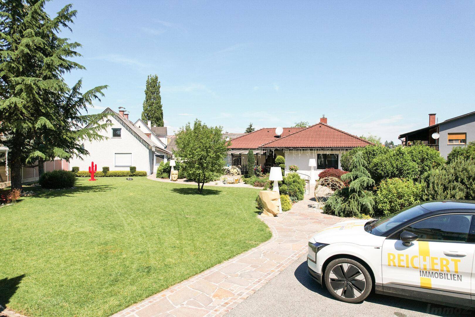 Gepflegter Gartenbereich mit großer Rasenfläche und einem modernen Haus im Hintergrund.