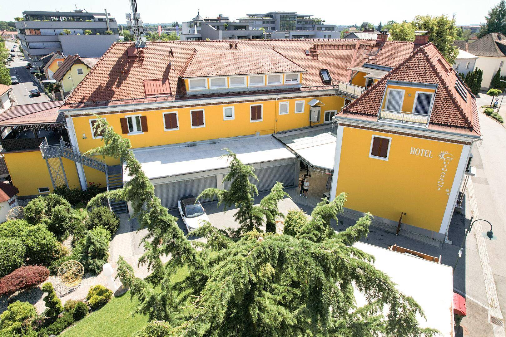 Luftaufnahme des großen gelben Hotelgebäudes mit roten Dächern, Parkplätzen und umliegender Vegetation.