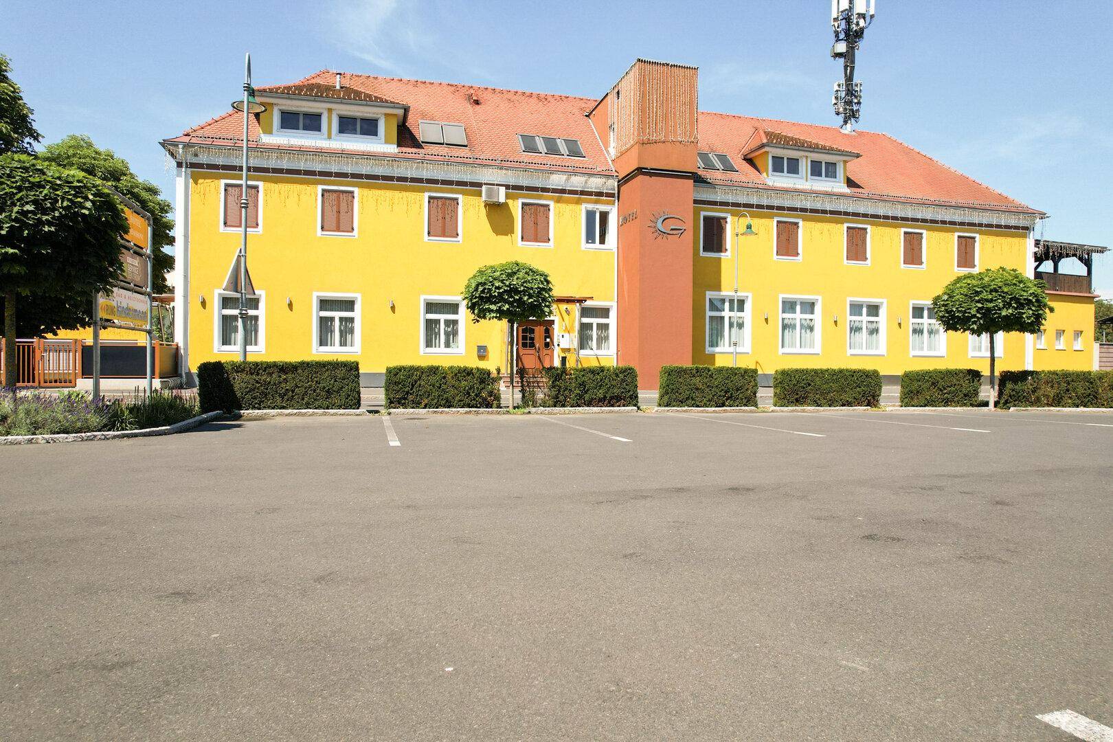Gesamtansicht des gelben Hotelgebäudes mit großem Parkplatz und gepflegten Hecken.