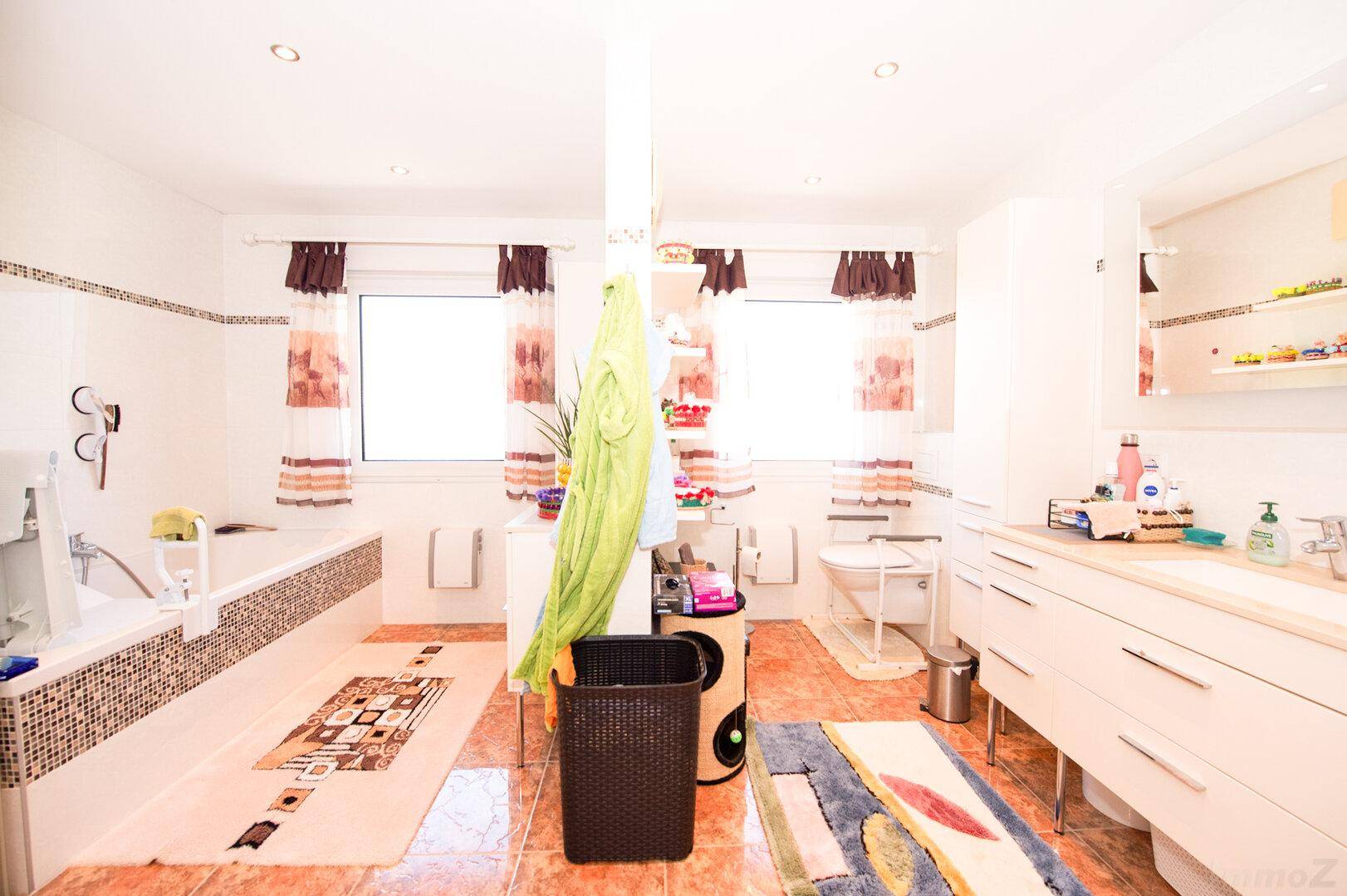 Helles und geräumiges Badezimmer mit Badewanne, Dusche, Doppelwaschbecken und zwei Fenstern.