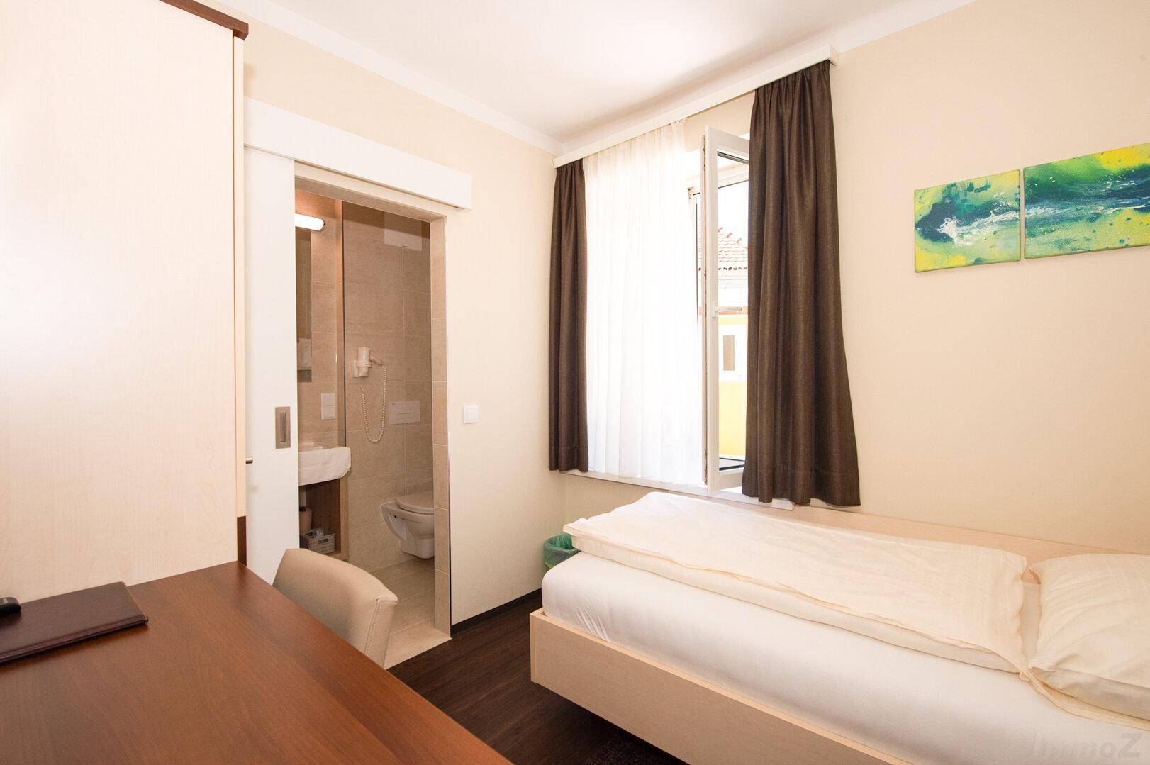 Gemütliches Schlafzimmer mit Einzelbett, Schreibtisch und Zugang zu einem privaten Badezimmer.