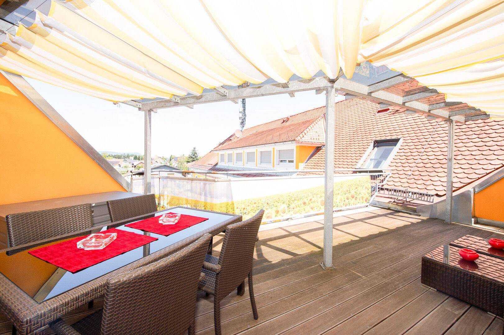 Geräumige Dachterrasse mit bequemen Rattanmöbeln und einem ausziehbaren Sonnenschutz.