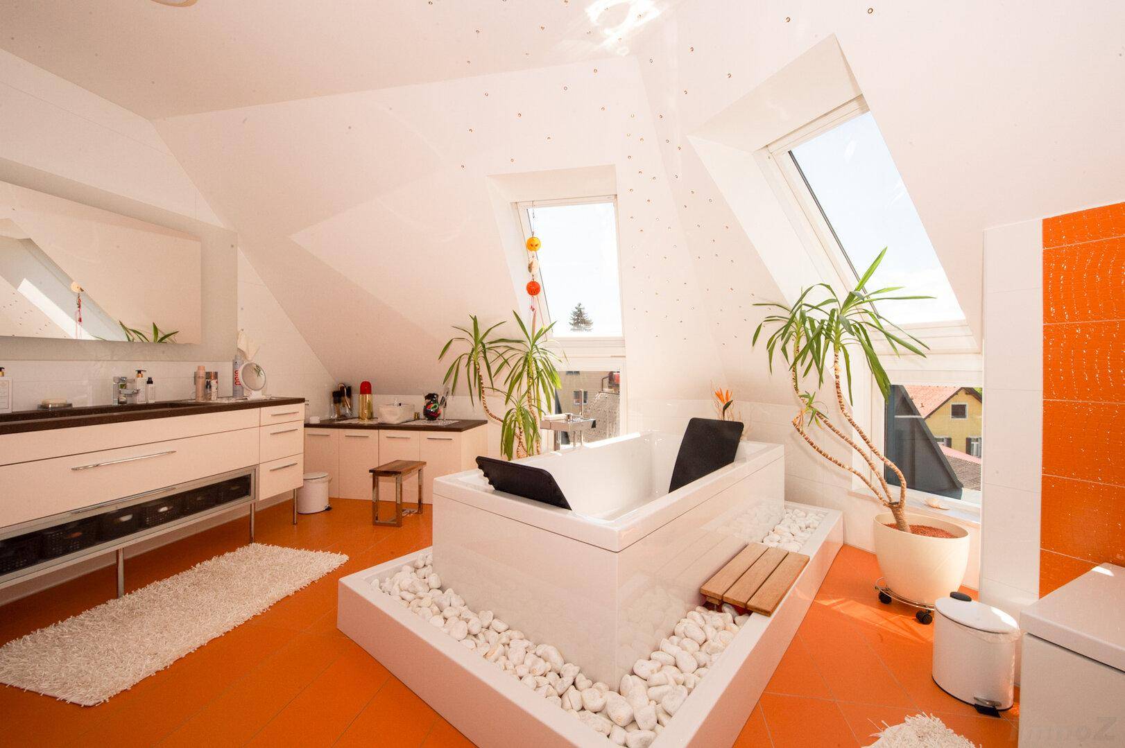 Modernes Badezimmer im Dachgeschoss mit freistehender Badewanne und orangefarbenen Akzenten.