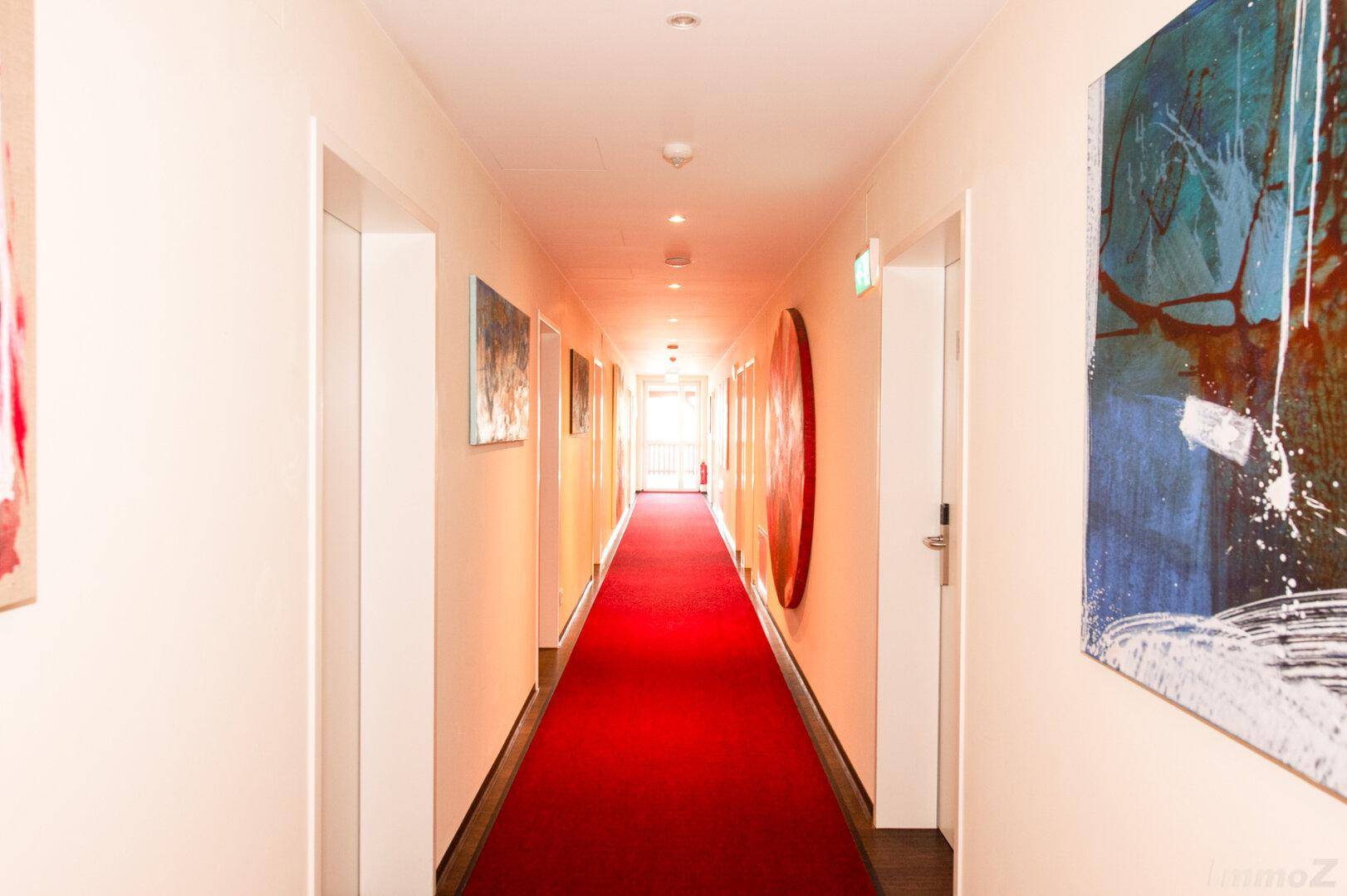 Langer, heller Flur mit rotem Teppich und modernen Kunstwerken an den Wänden.