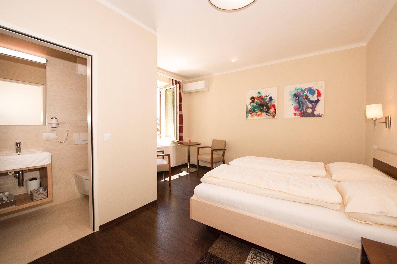 Helles Schlafzimmer mit zwei Einzelbetten, kleinem Tisch und direktem Zugang zum Badezimmer.