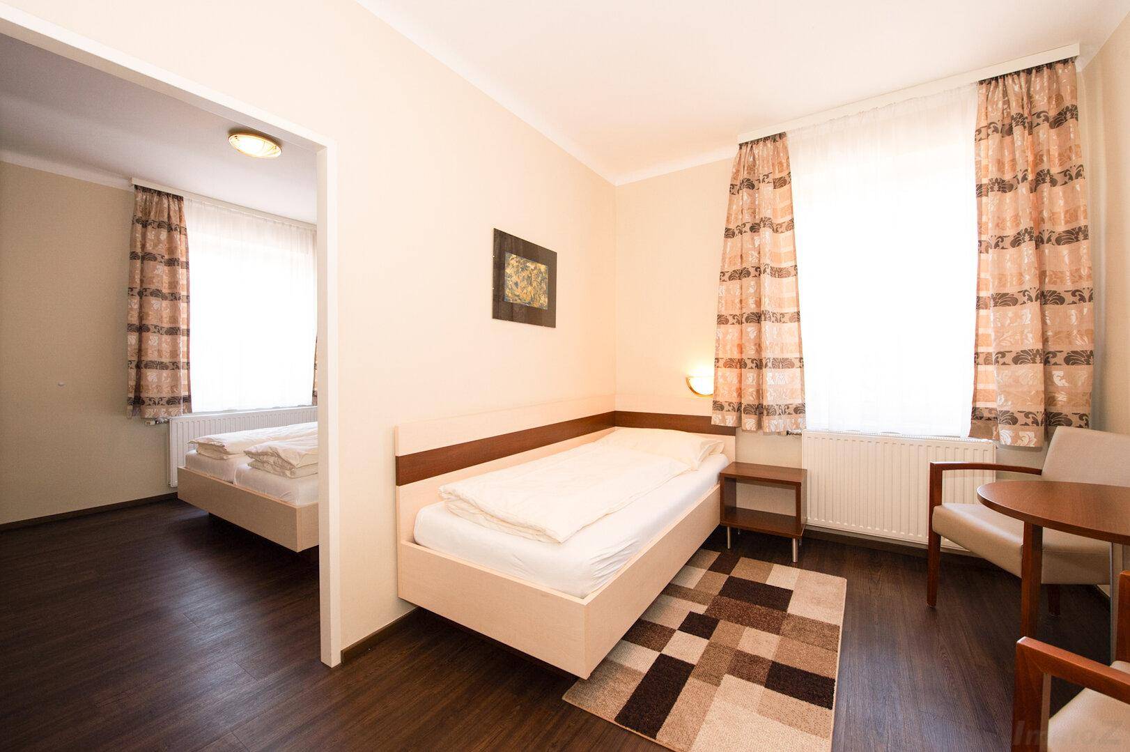 Helles Schlafzimmer mit zwei Einzelbetten und einem kleinen Tisch, angrenzend an einen weiteren Raum.