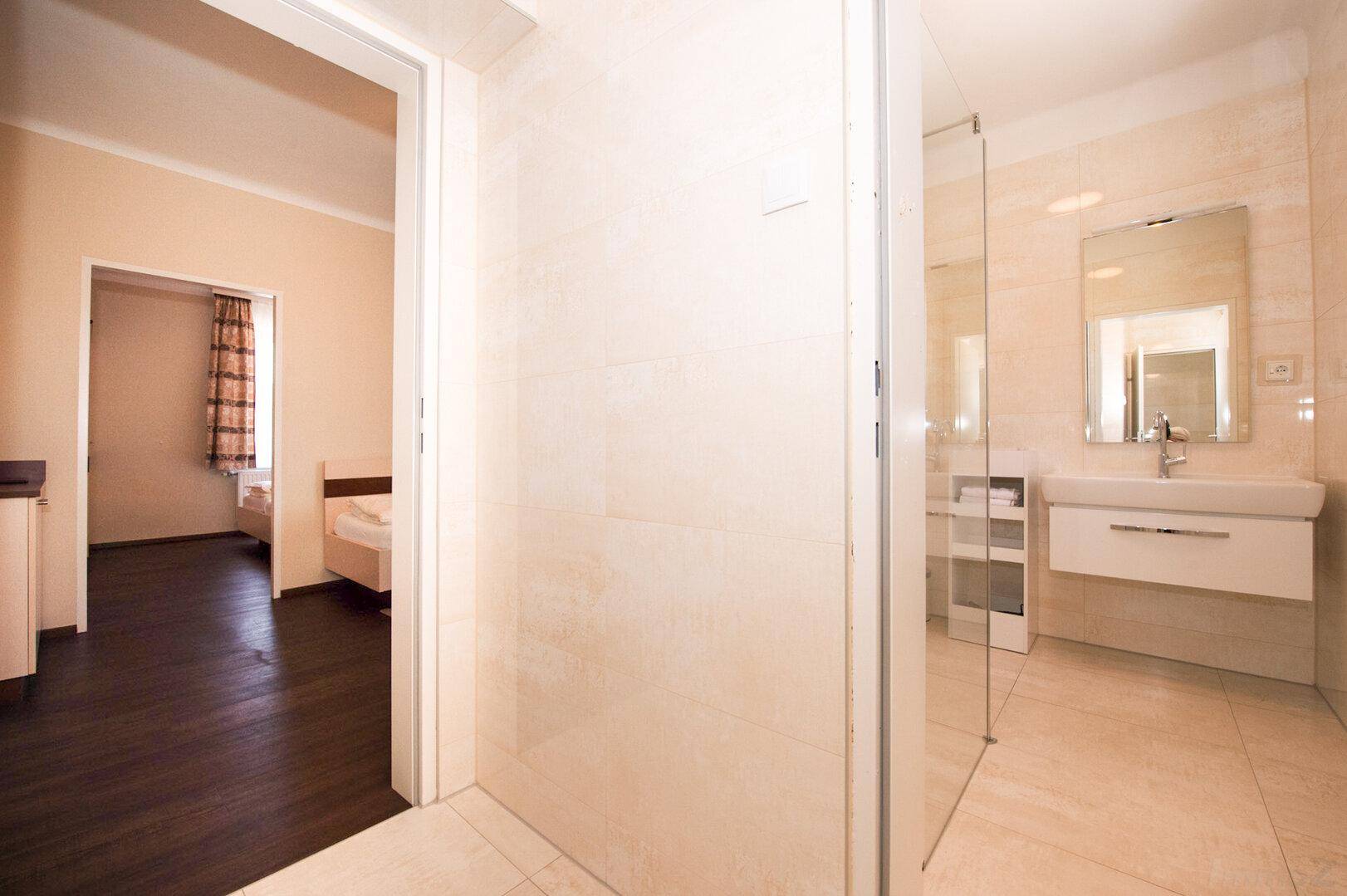 Geräumiges Badezimmer mit Duschkabine, modernem Waschbecken und Blick in ein Schlafzimmer.