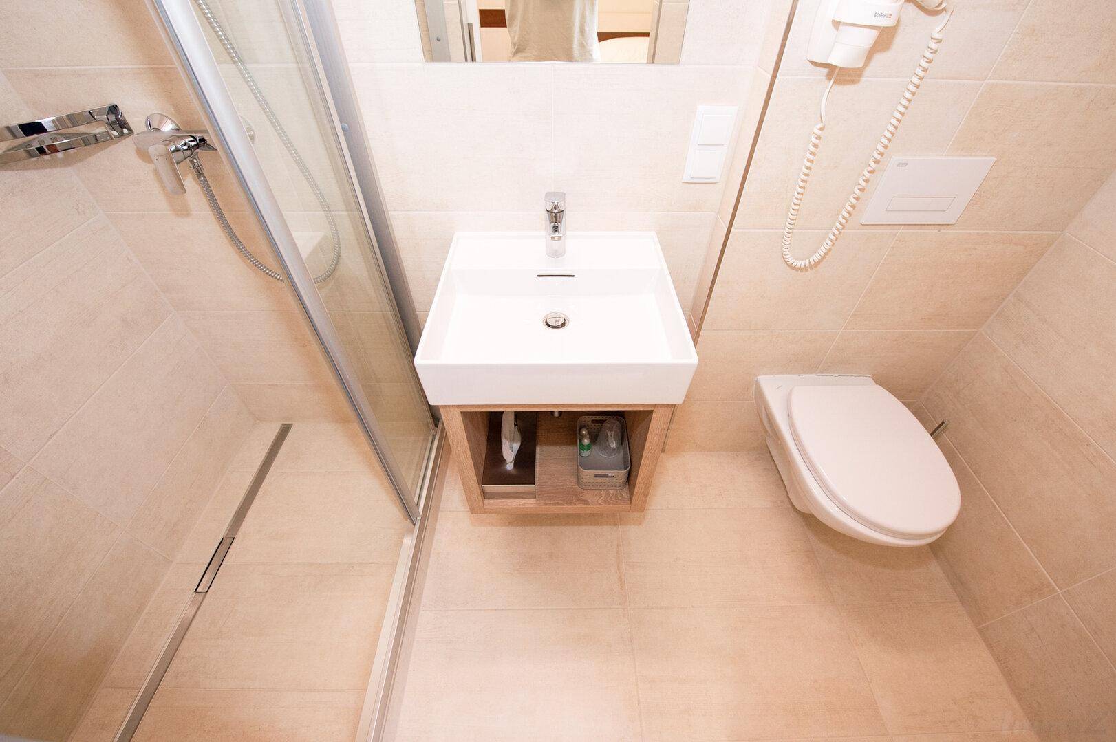 Modernes Badezimmer mit ebenerdiger Dusche, Waschbecken und wandhängendem WC.