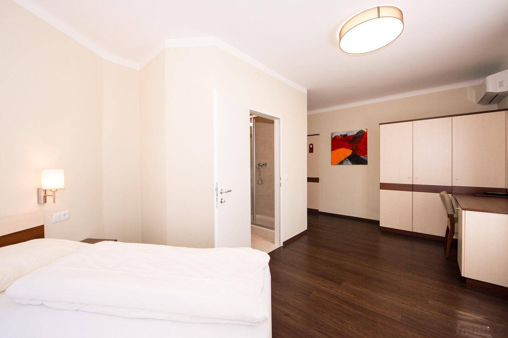Helles Schlafzimmer mit Doppelbett, Kleiderschrank, Schreibtisch und angrenzendem Badezimmer.