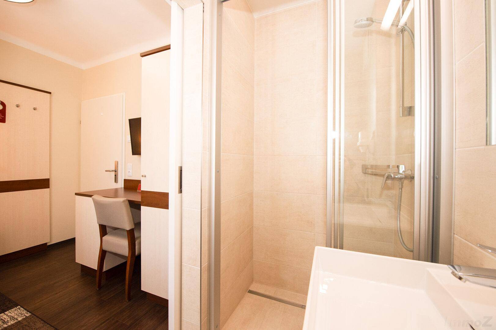 Kompaktes Badezimmer mit Duschkabine, Waschbecken und Blick auf einen Arbeitsbereich.