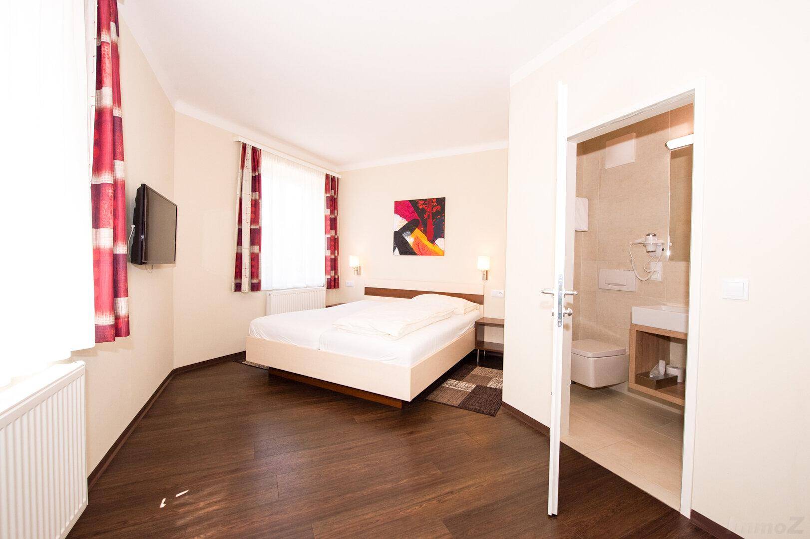 Geräumiges Schlafzimmer mit Doppelbett, Fernseher und direktem Zugang zu einem Badezimmer.