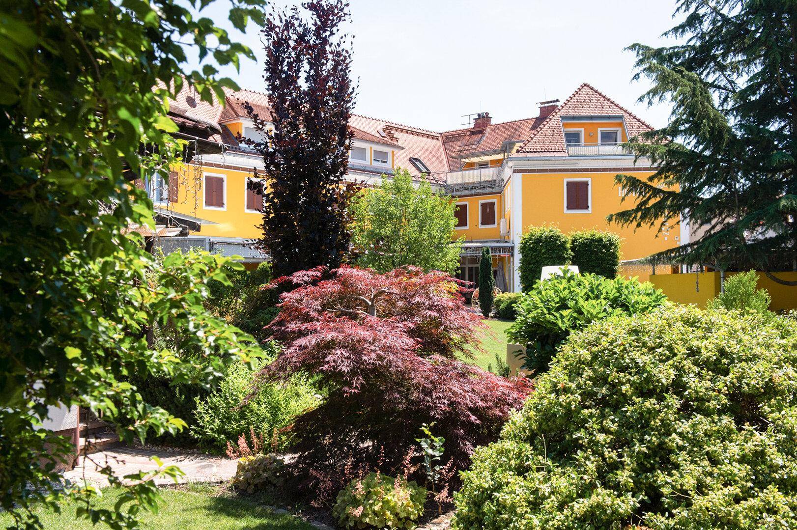 Gepflegter Gartenbereich mit vielfältiger Bepflanzung und Blick auf das gelbe Hotelgebäude.
