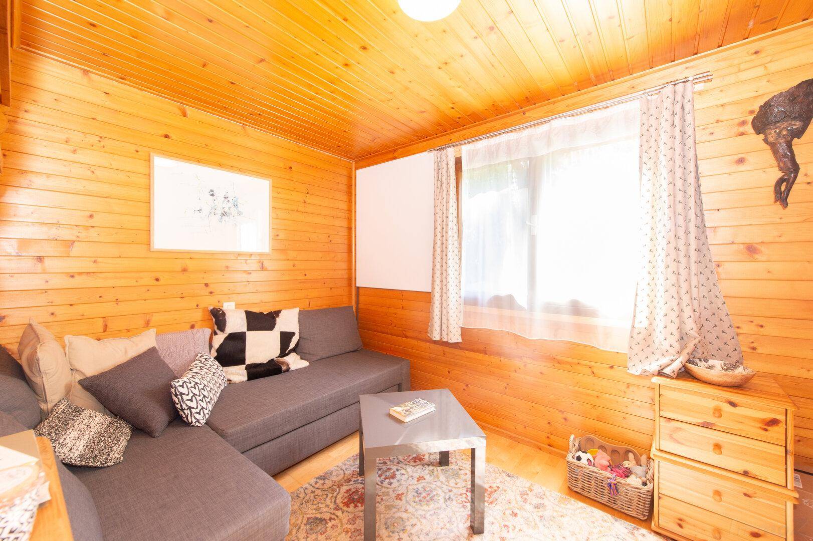 Helles Wohnzimmer mit Holzwänden, bequemer Couch und einem Fenster mit Vorhängen.