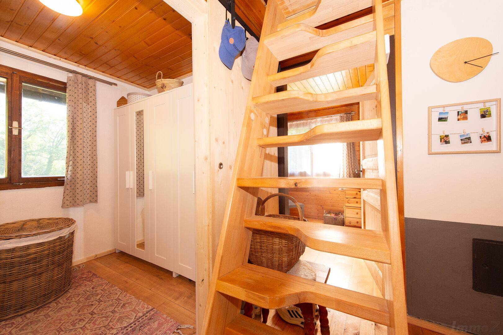 Flur mit schmaler Holztreppe, weißen Schränken und Holzboden.