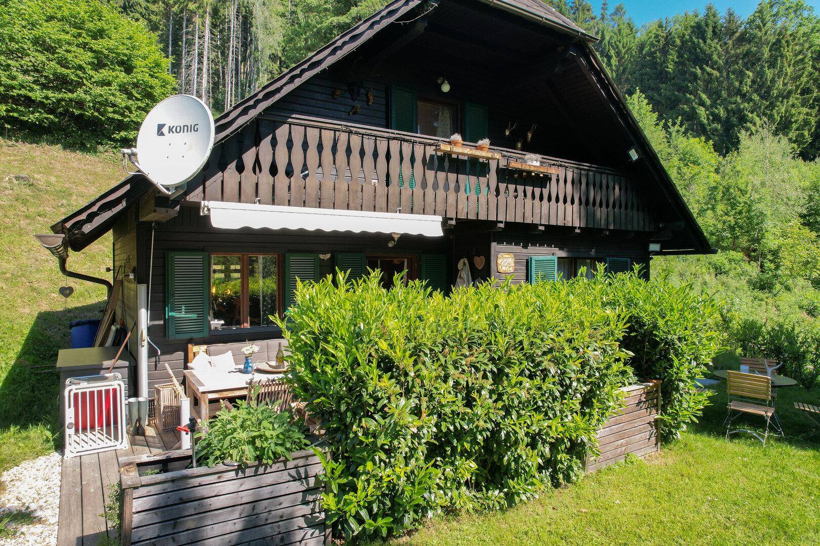 Detailansicht des Holzhauses mit Balkon, Satellitenschüssel und einer gemütlichen Terrasse.