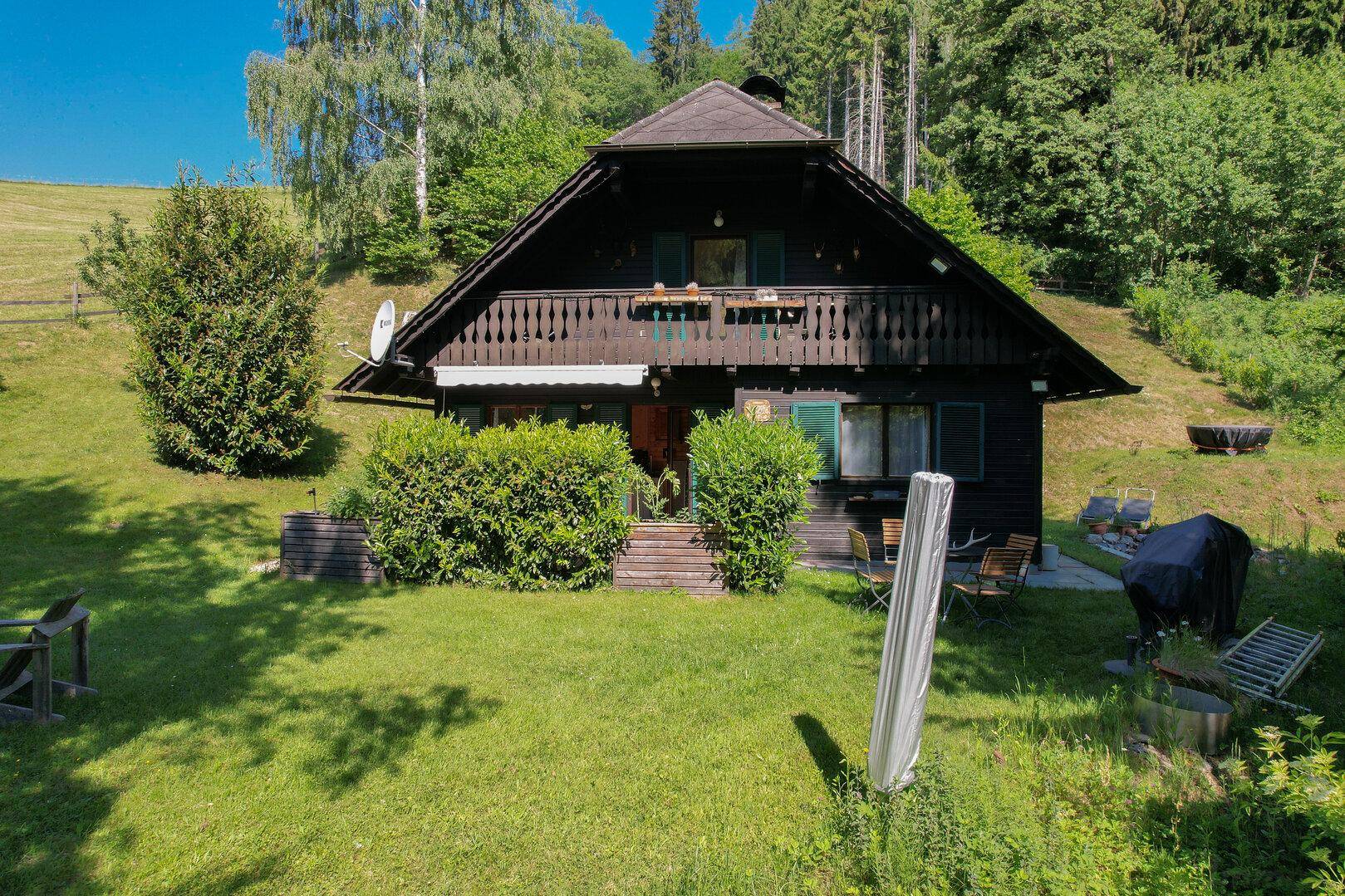 Idyllisches Holzhaus mit großem Garten, umgeben von üppiger grüner Natur und Wald.