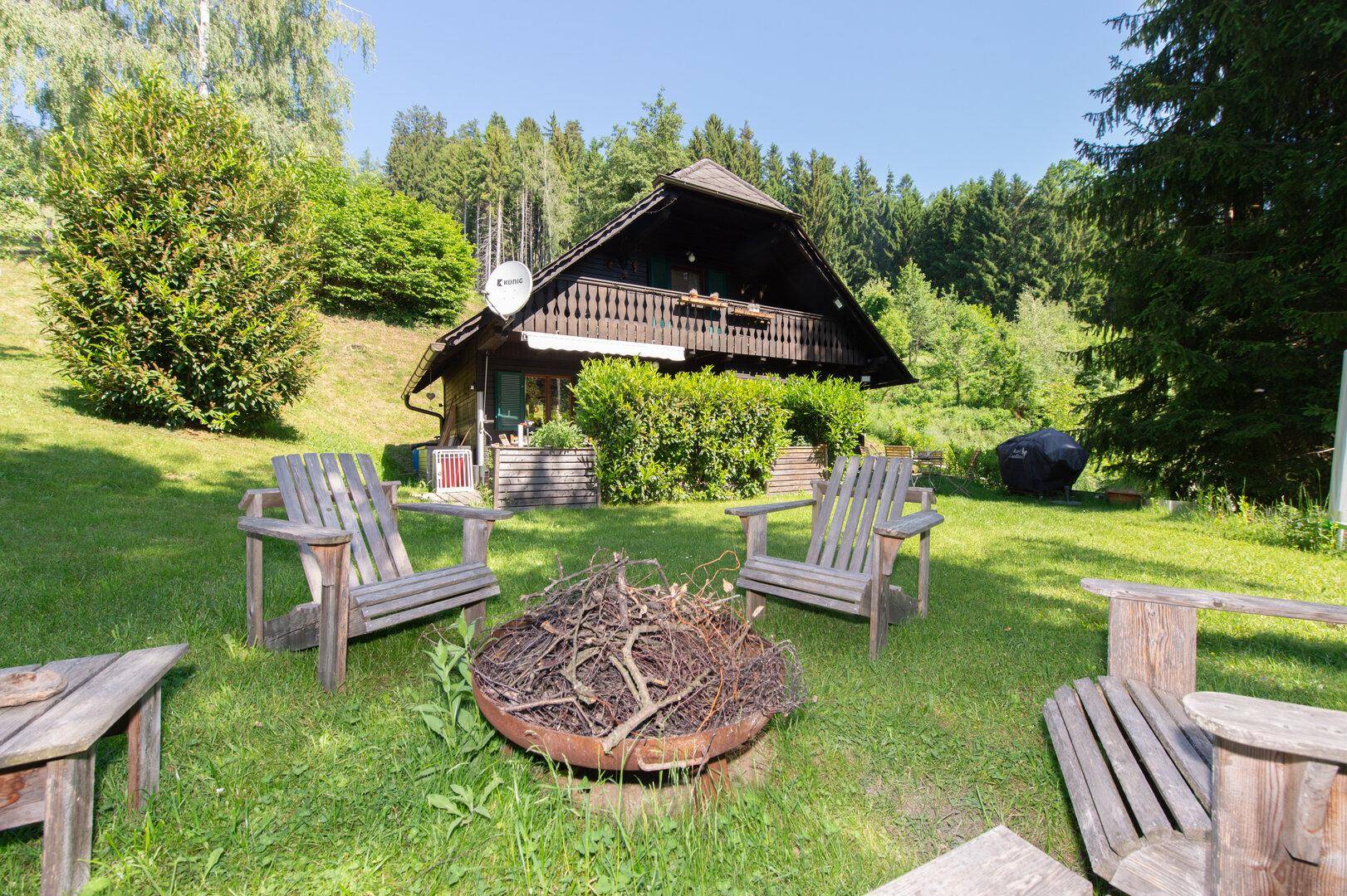 Gemütliche Feuerstelle mit Holzstühlen im Garten vor dem traditionellen Holzhaus.