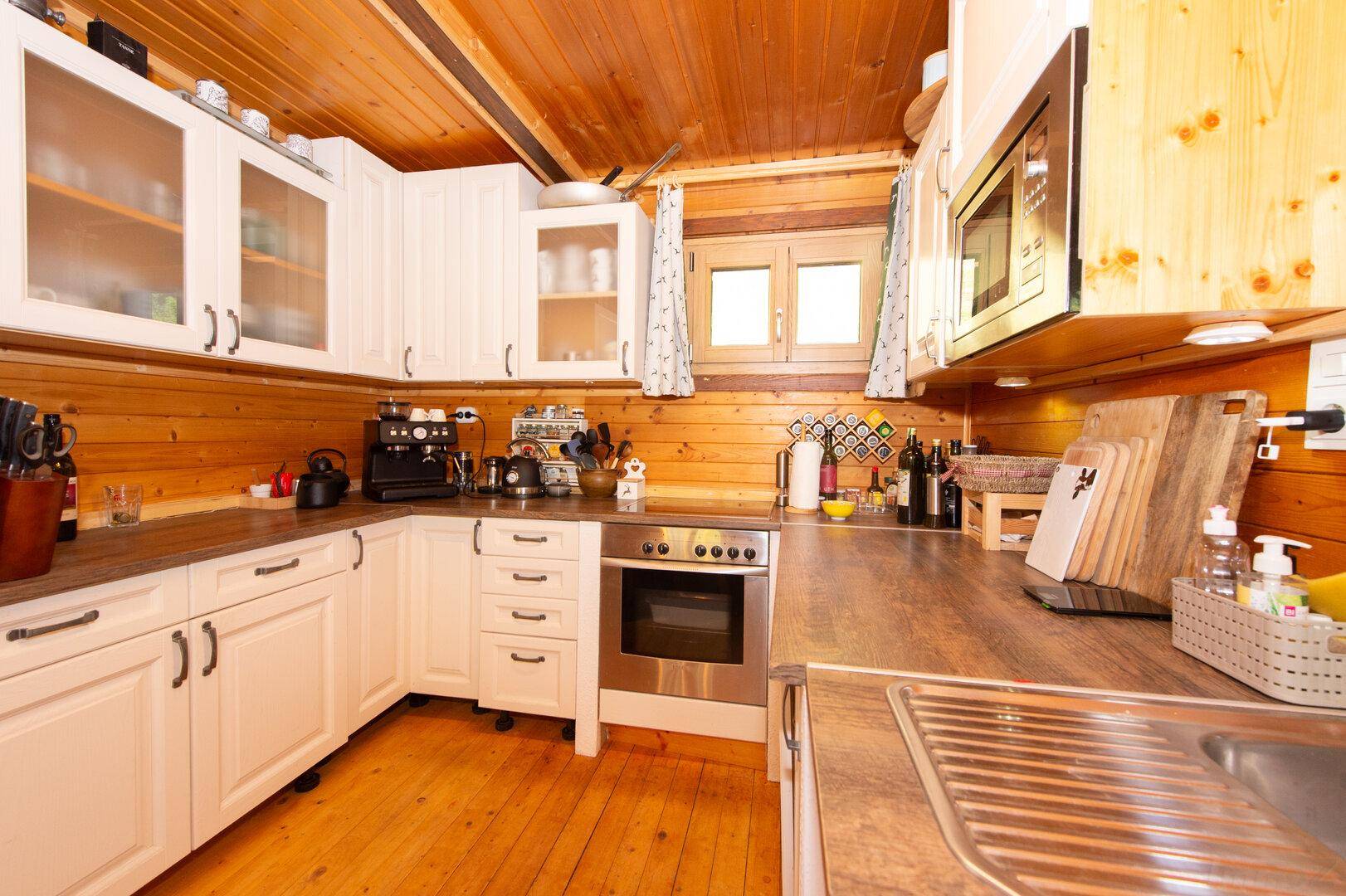 Funktionale Küche mit Holzwänden, weißen Schränken, Backofen und Mikrowelle.