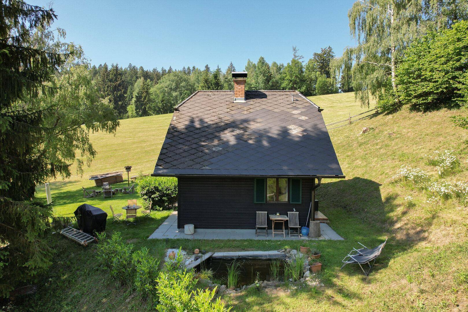 Rückansicht des Hauses mit kleiner Terrasse, Teich und weitläufigem Gartenbereich.