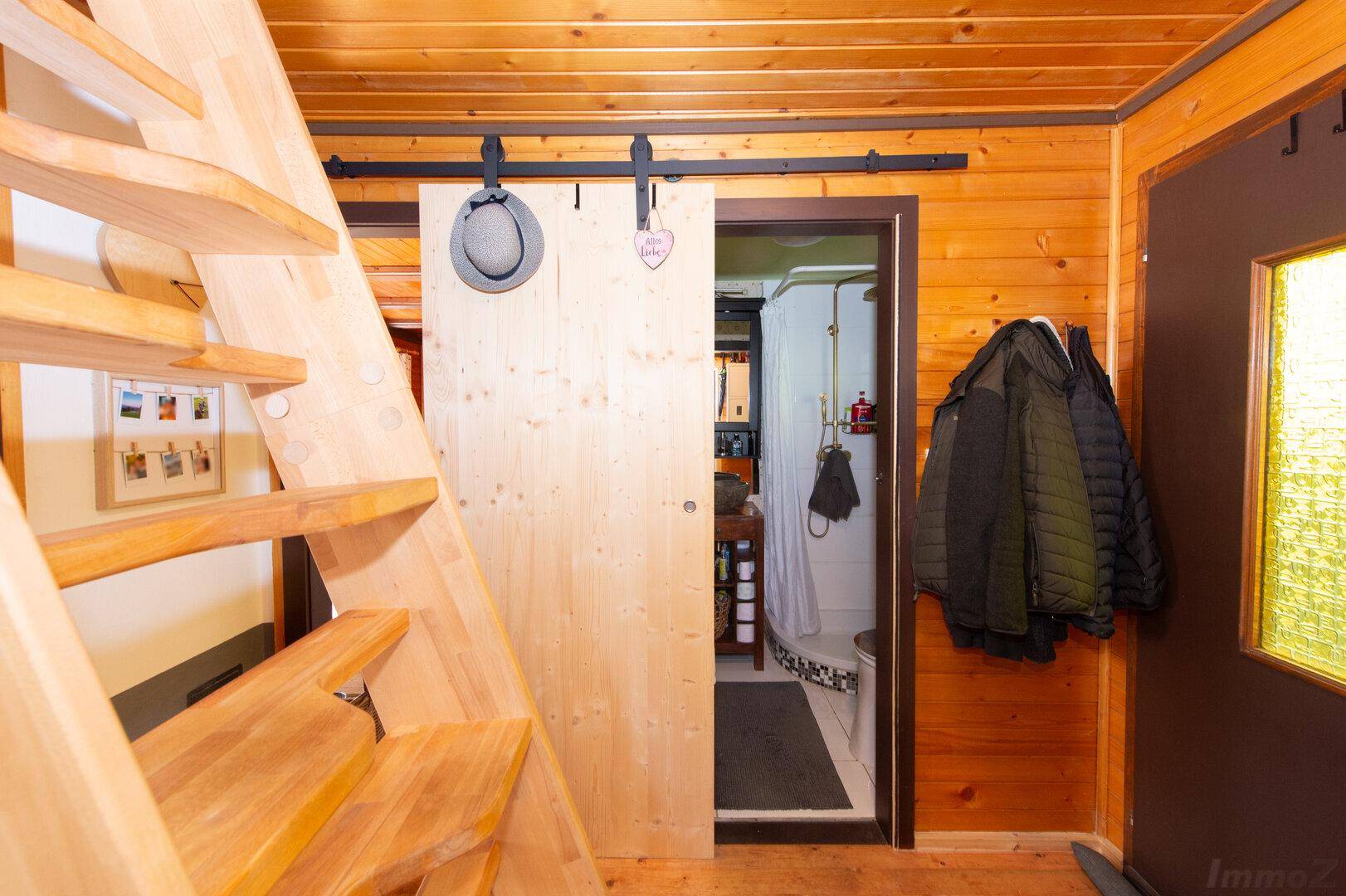 Rustikaler Eingangsbereich mit Holztreppe, Holzwänden und einer Schiebetür zum Badezimmer.