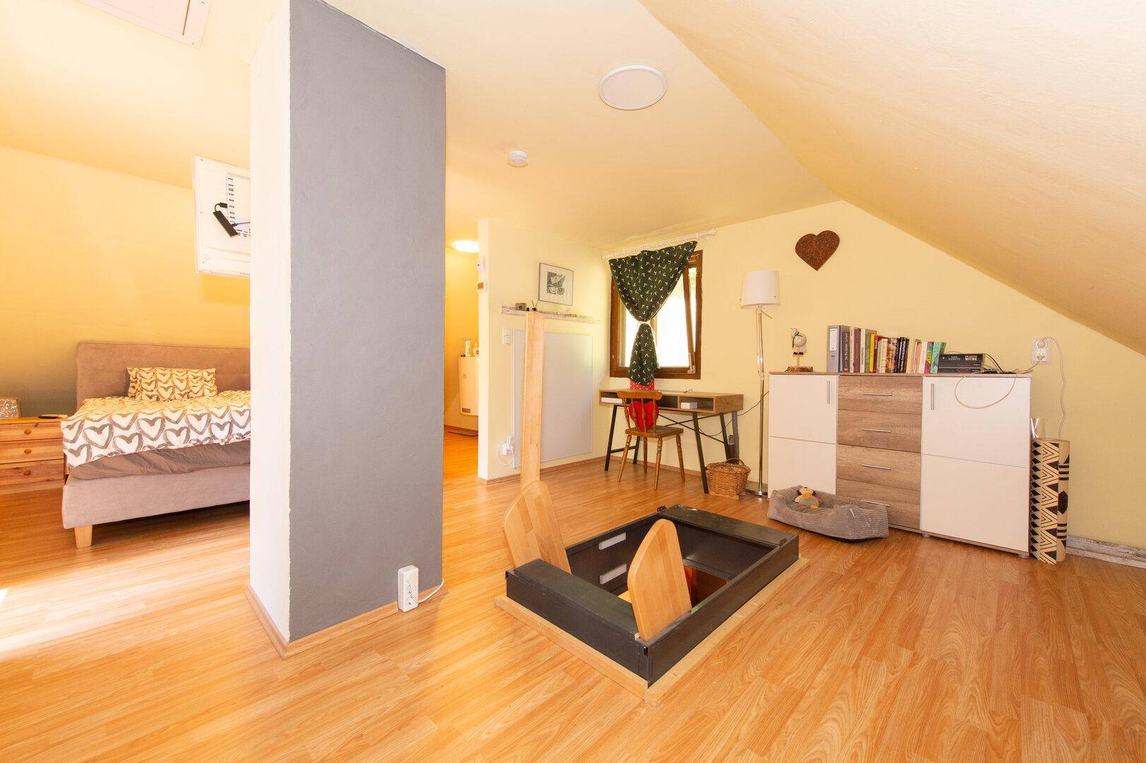 Geräumiges Schlafzimmer im Dachgeschoss mit Holzboden, schrägen Wänden und viel Tageslicht.