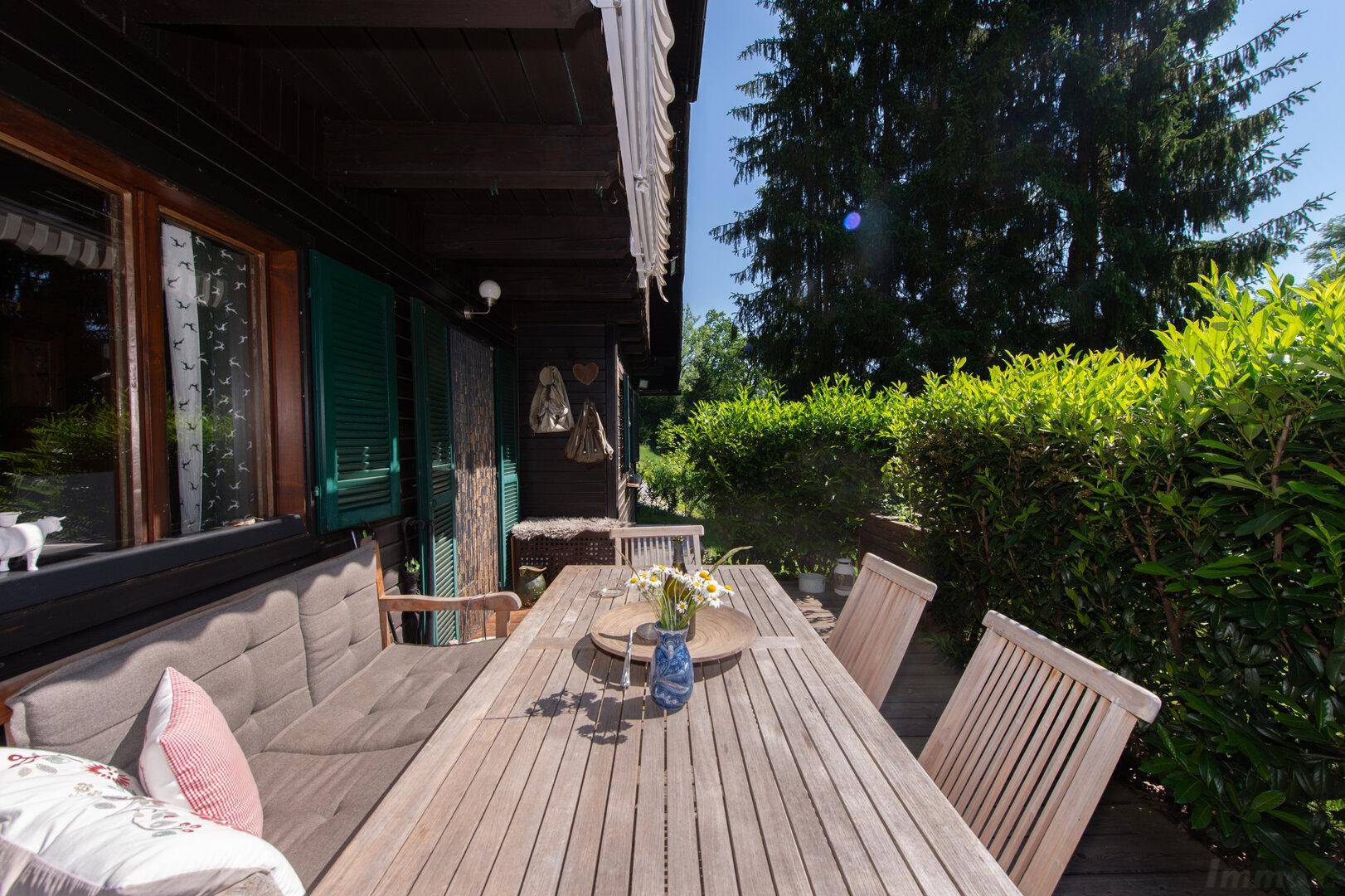 Sonnige Holzterrasse mit bequemen Gartenmöbeln und Blick ins Grüne, ideal zum Entspannen.
