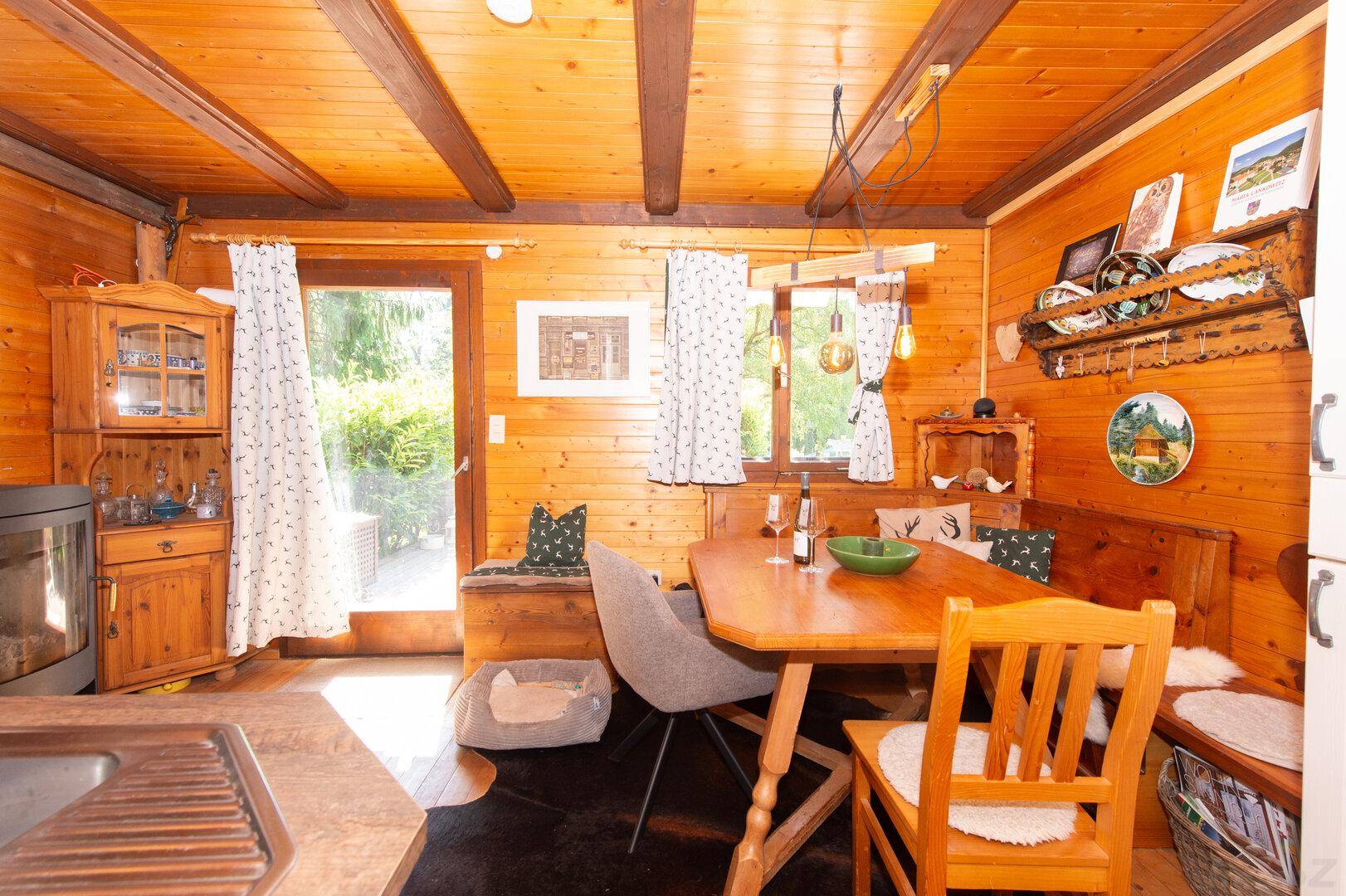 Offener Wohn- und Essbereich mit Holzwänden, Kaminofen und Zugang zur Terrasse.