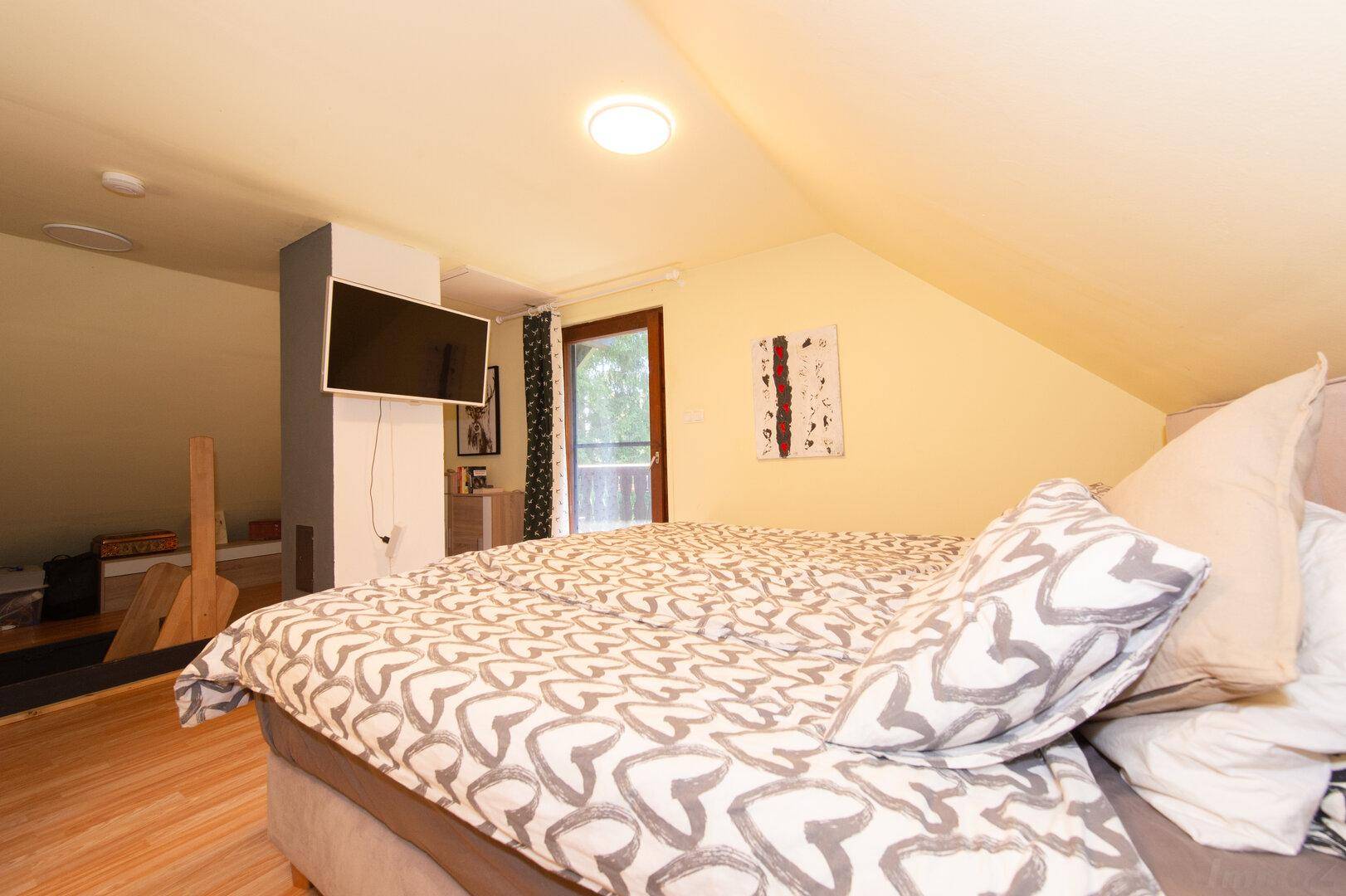 Dachgeschoss-Schlafzimmer mit Fernseher, Bett und Zugang zu einem kleinen Balkon.