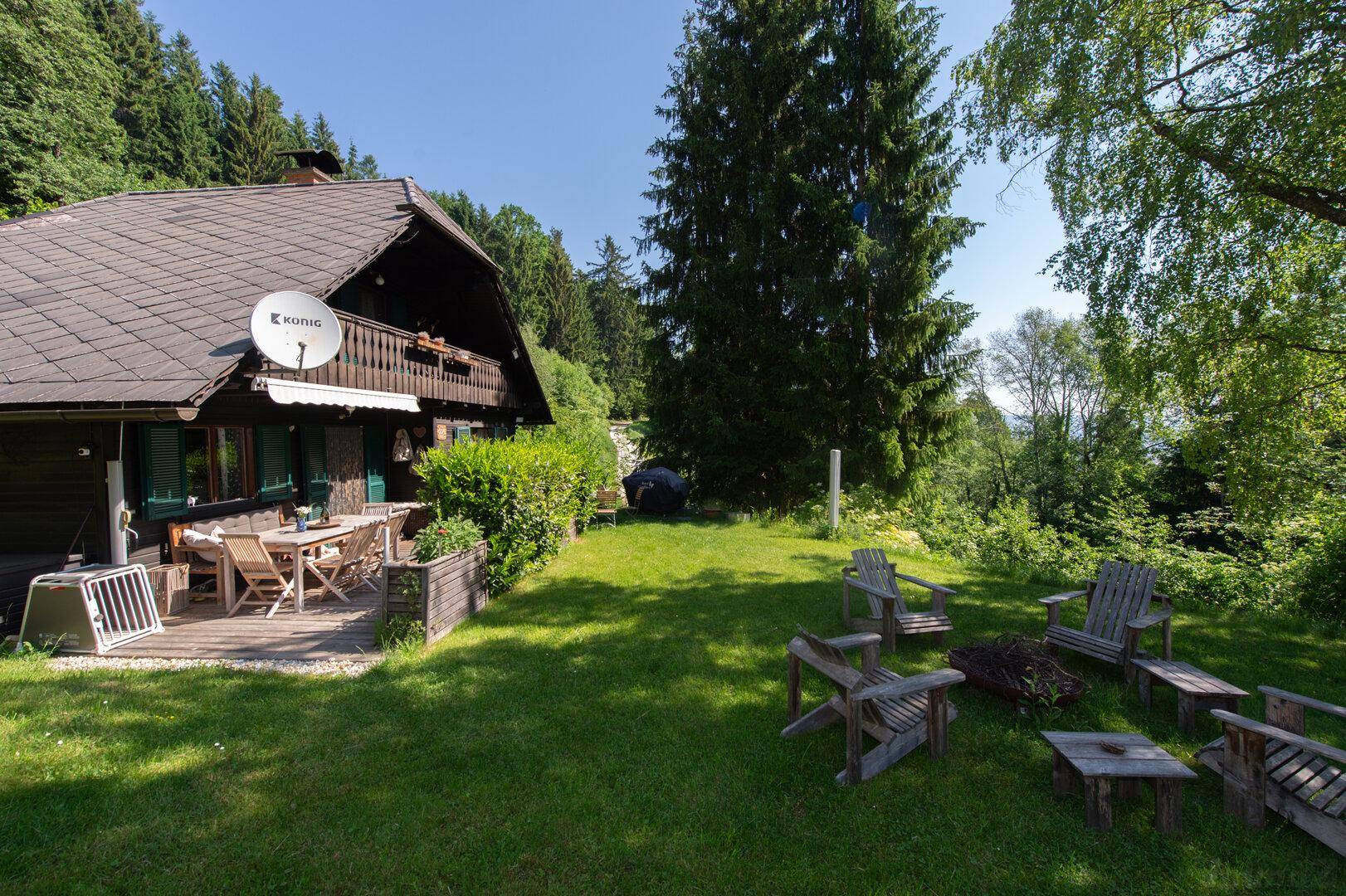 Weitläufiger Gartenbereich mit Terrasse und Feuerstelle, umgeben von grüner Natur.