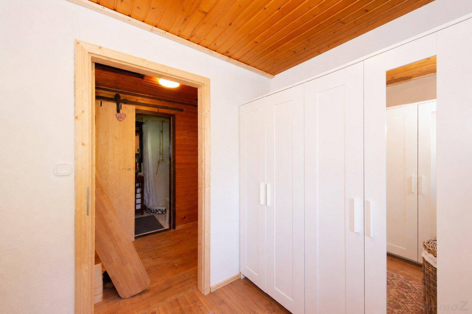 Flur mit Holzdecke und -boden, weißen Schränken und einer rustikalen Schiebetür.